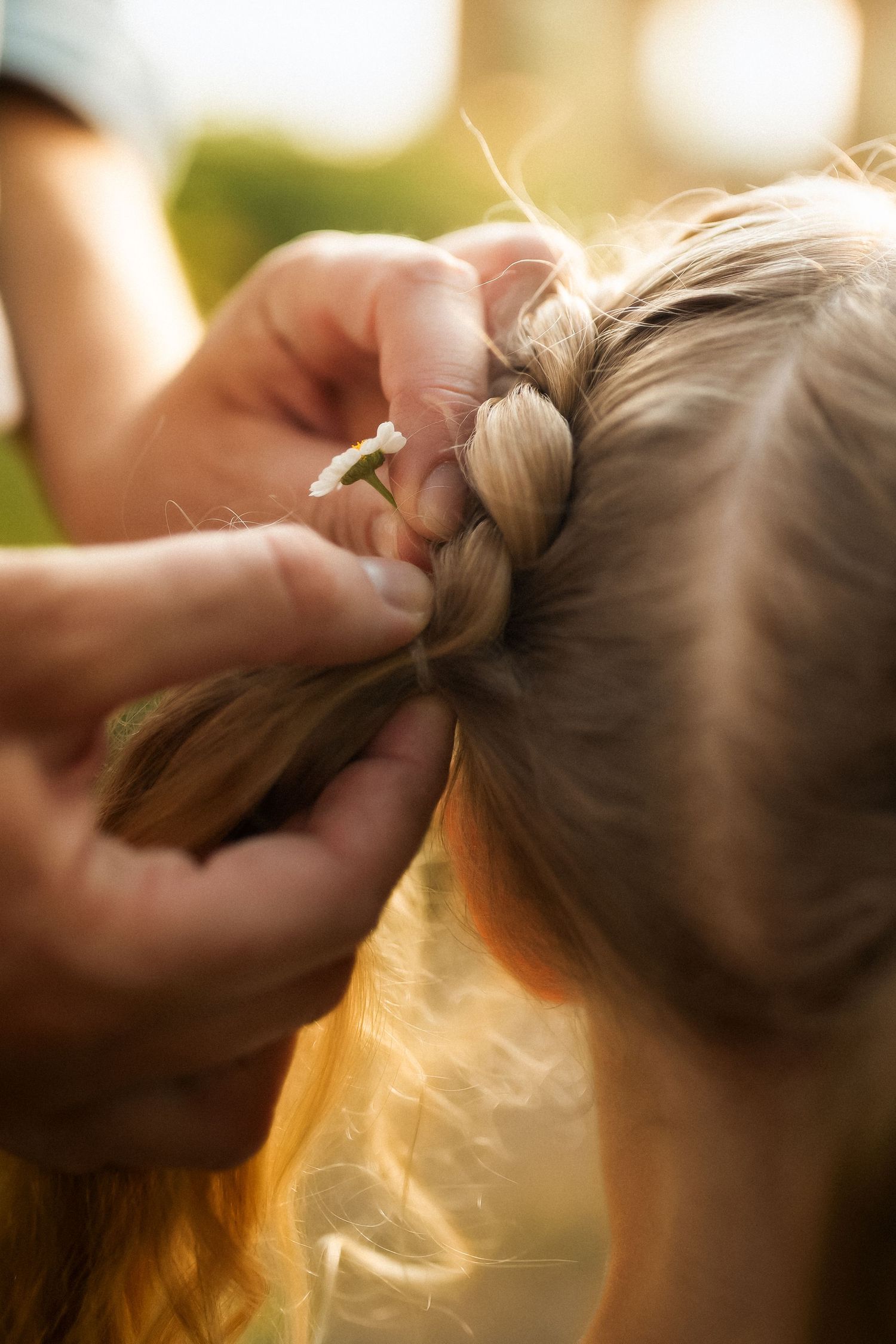 Close-up sequence showing hands styling long blonde hair into a bun against a warm sunlit background.
