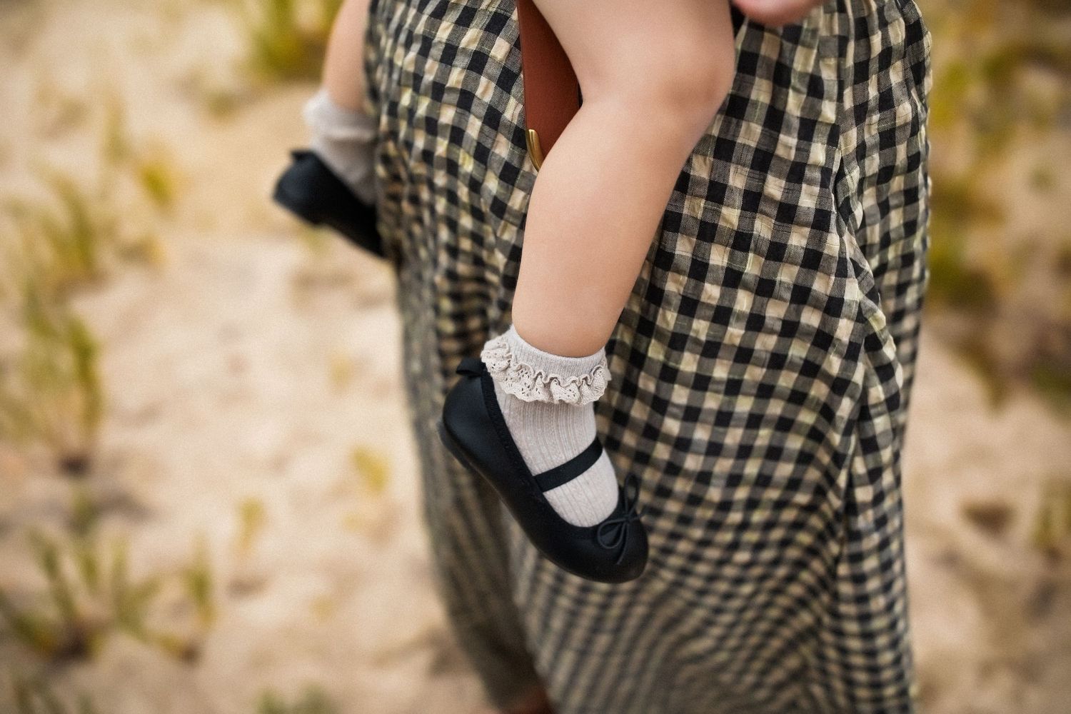 Close-up of small feet wearing white lace socks and black shoes against gingham pattern dress.