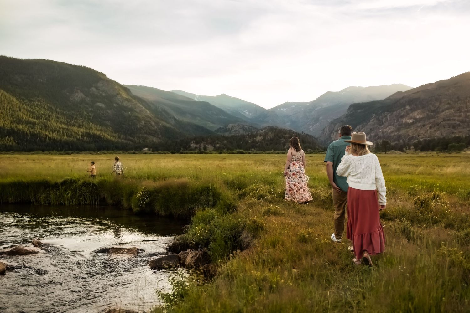 A scenic mountain landscape with figures walking through a golden meadow at sunset.