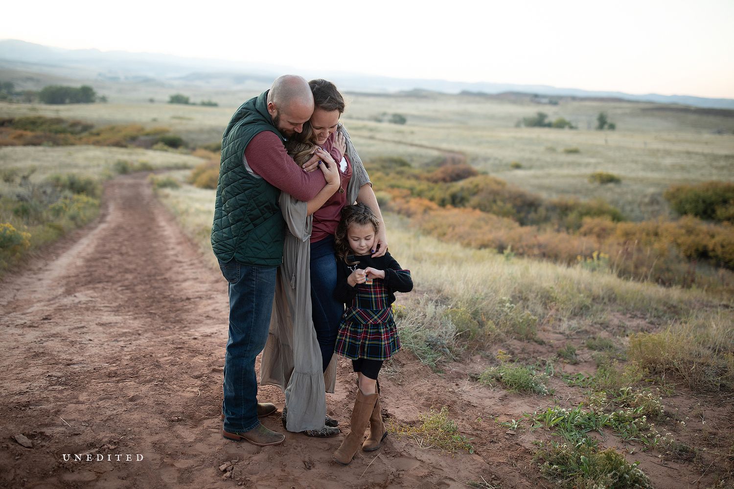 Family walking together on a dirt path through rolling hills at sunset.
