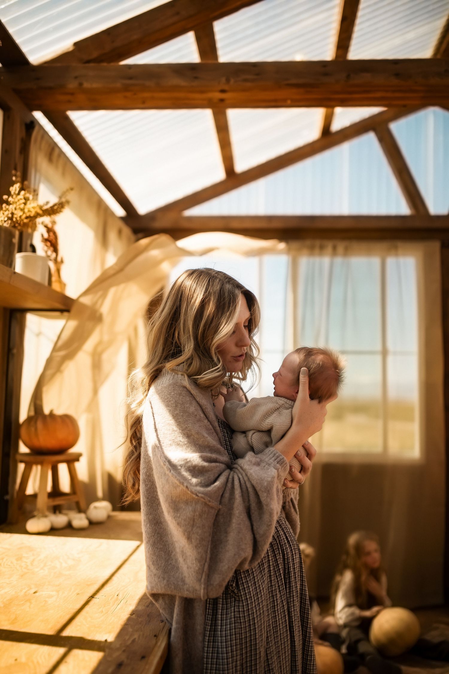 Sunlit rustic room with wooden beams where a figure cradles a baby.