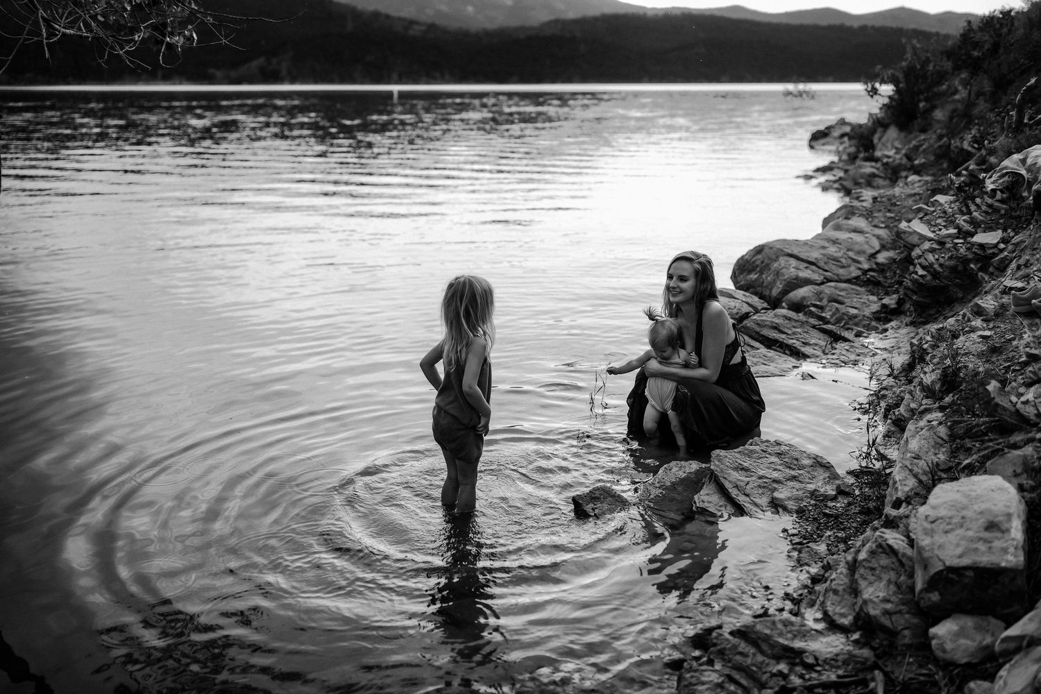 A serene black and white photograph of a tranquil moment by a lake with rippling water and rocky shoreline.