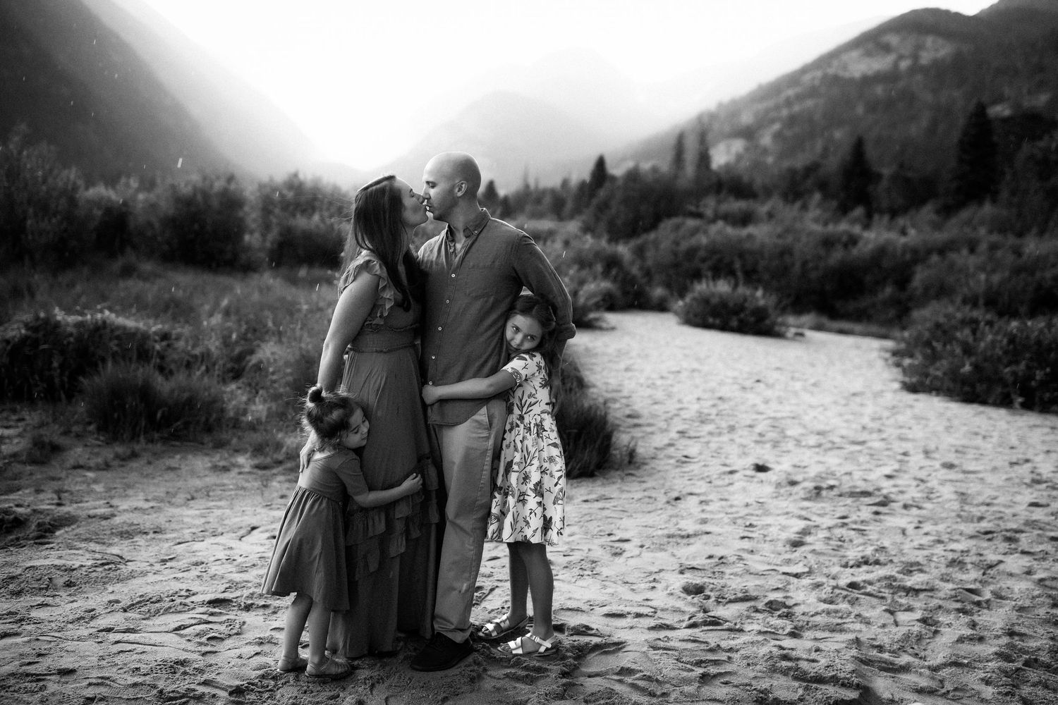 Black and white portrait of tender family moment against mountain landscape.