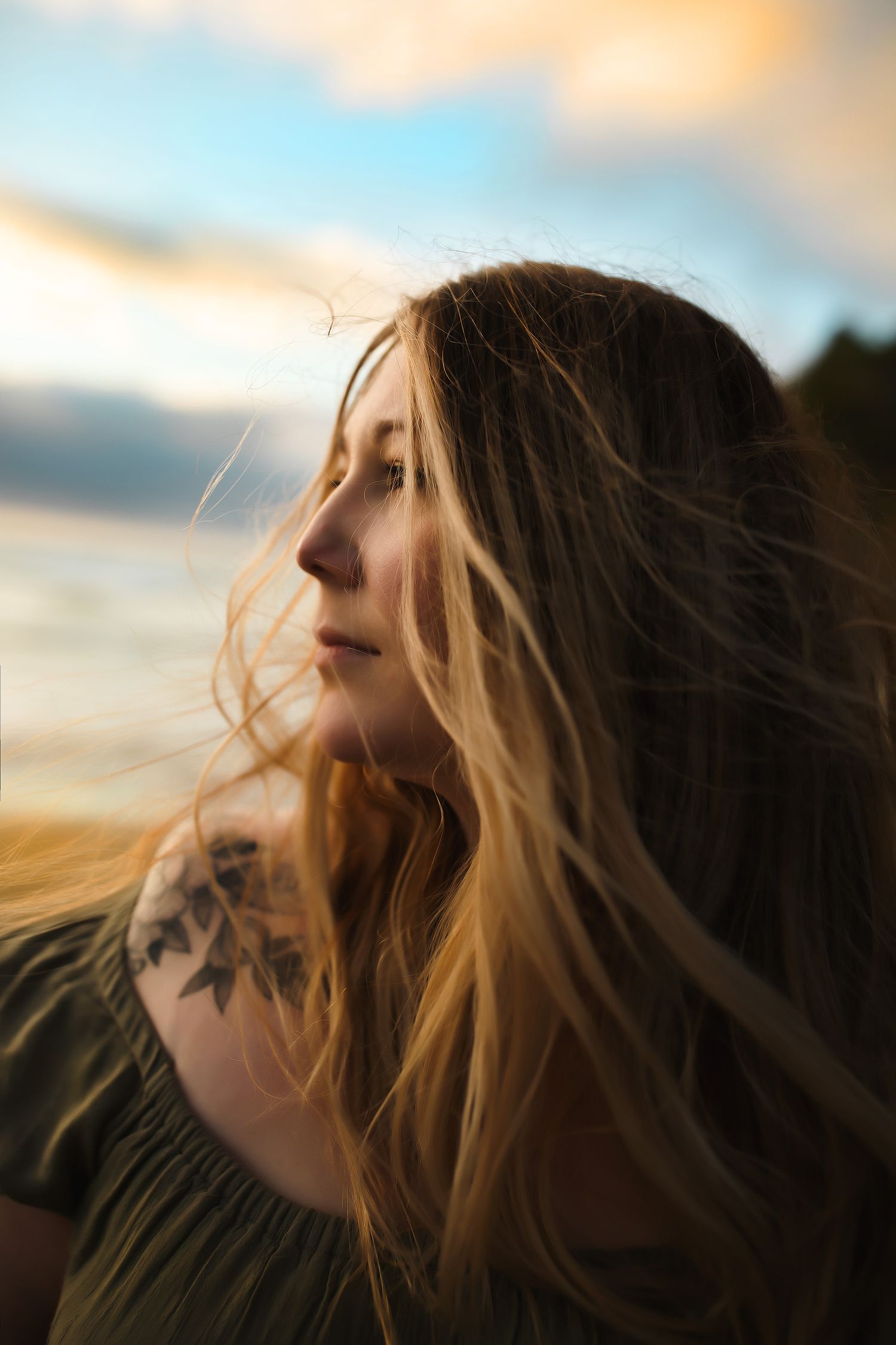 Profile view of person with blonde hair and shoulder tattoo against sunset sky.