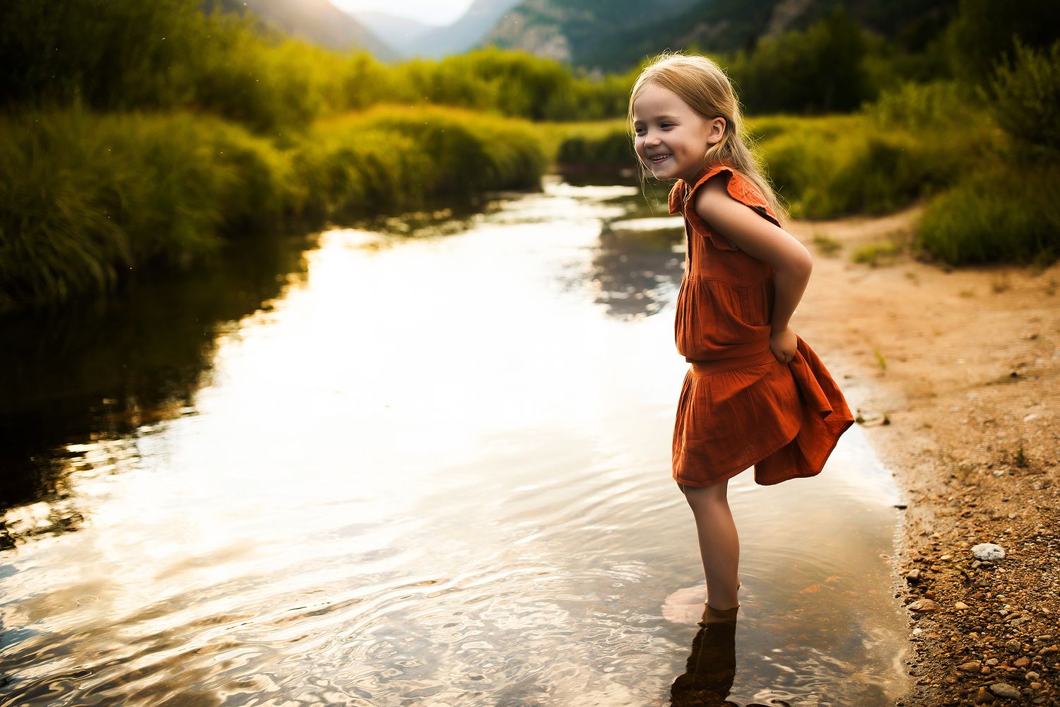 A person in a rust-colored dress splashes playfully in a sunlit river on a warm summer evening.