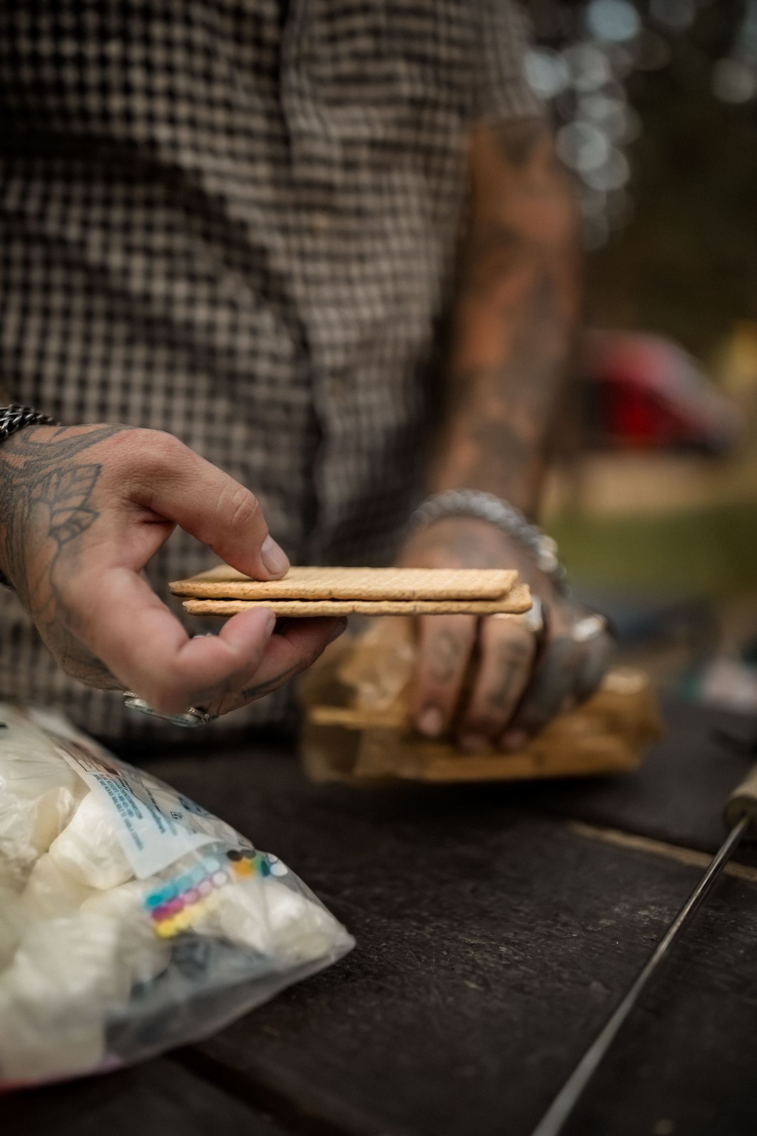 Hands preparing s'mores ingredients on a dark surface with graham crackers and marshmallows.