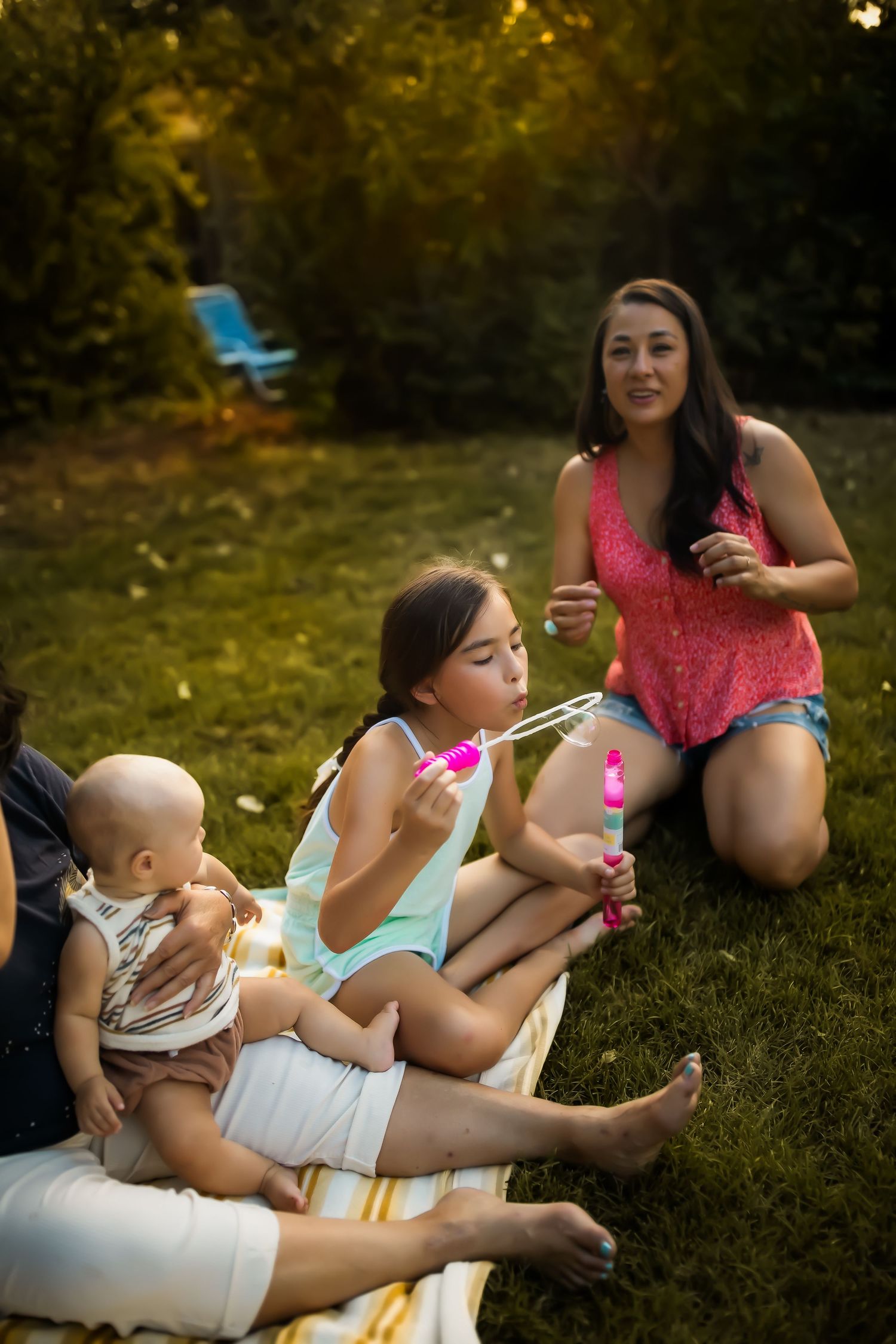 A group enjoys blowing bubbles together while relaxing on a blanket in a backyard on a summer evening.