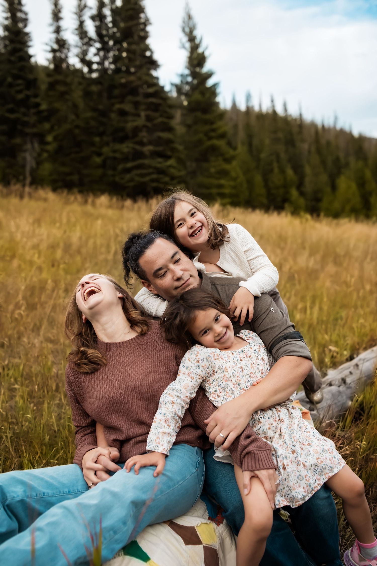 Candid moments of joy and laughter shared on a blanket in a mountain meadow.