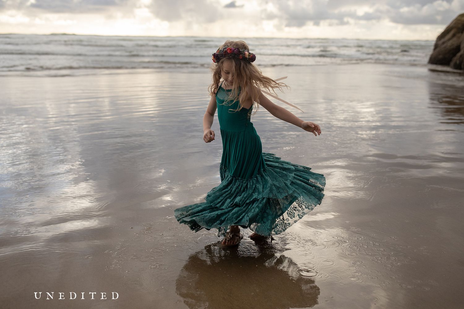 Woman in teal dress dances along misty coastline with dramatic cliffs and ocean waves.