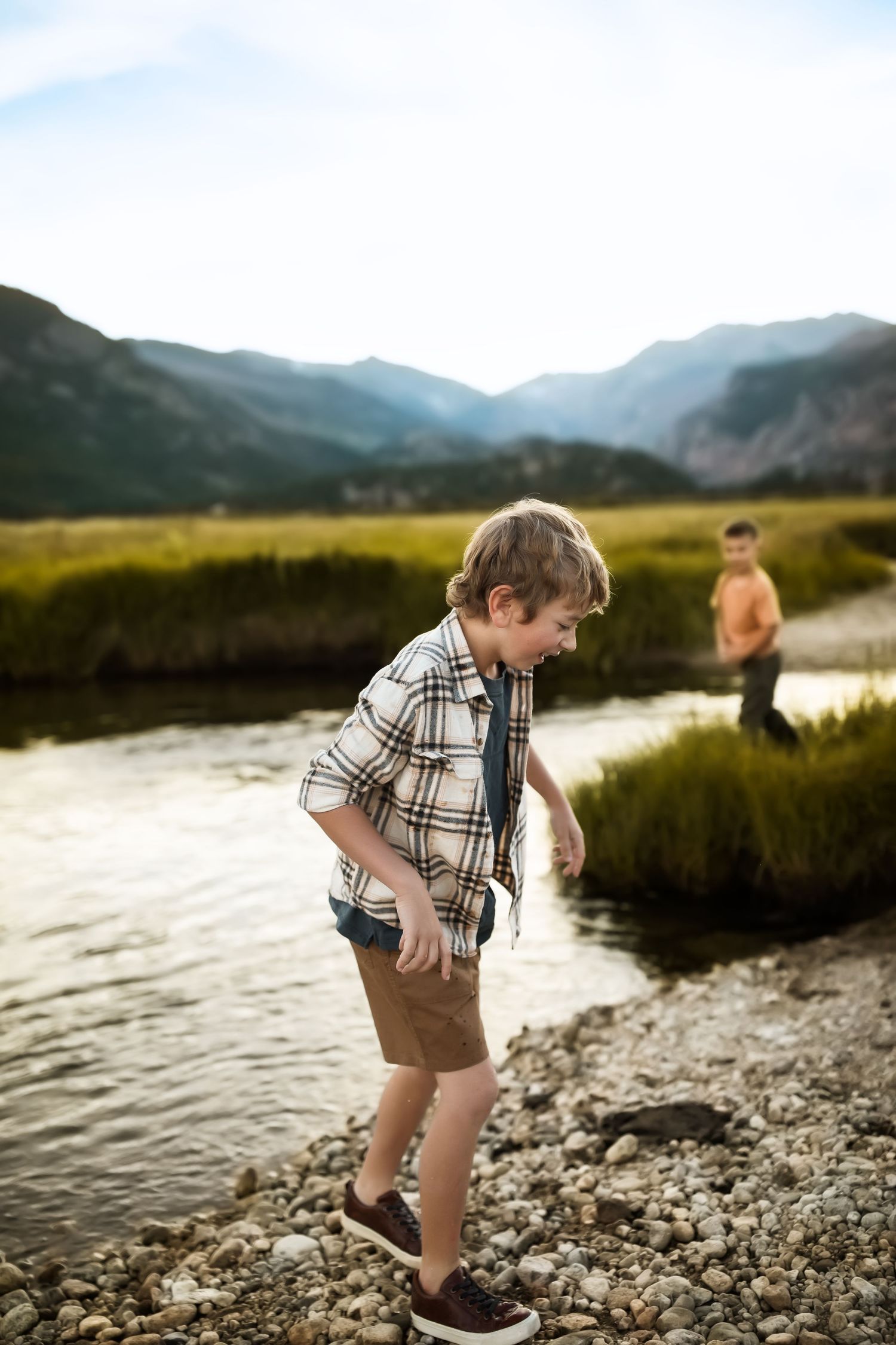 Person exploring rocky riverbank with mountain landscape in background at sunset.