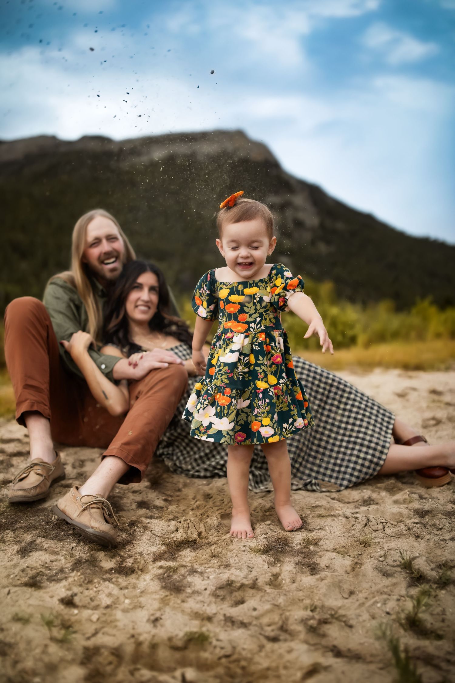 A playful family moment captured on sandy ground with mountains in the background.