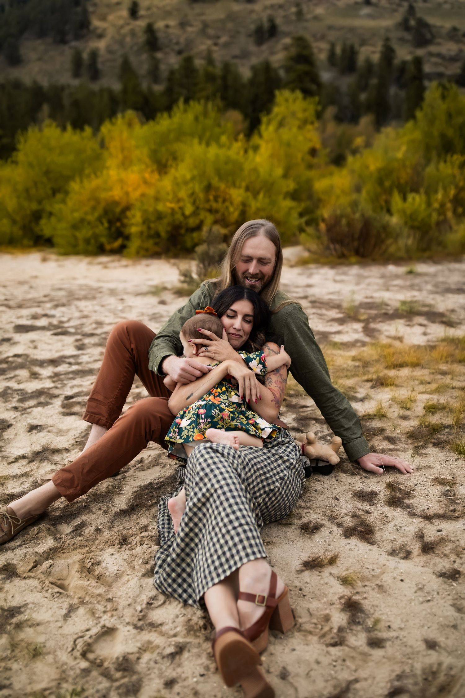 A couple embracing on sandy ground with autumn foliage in the background.