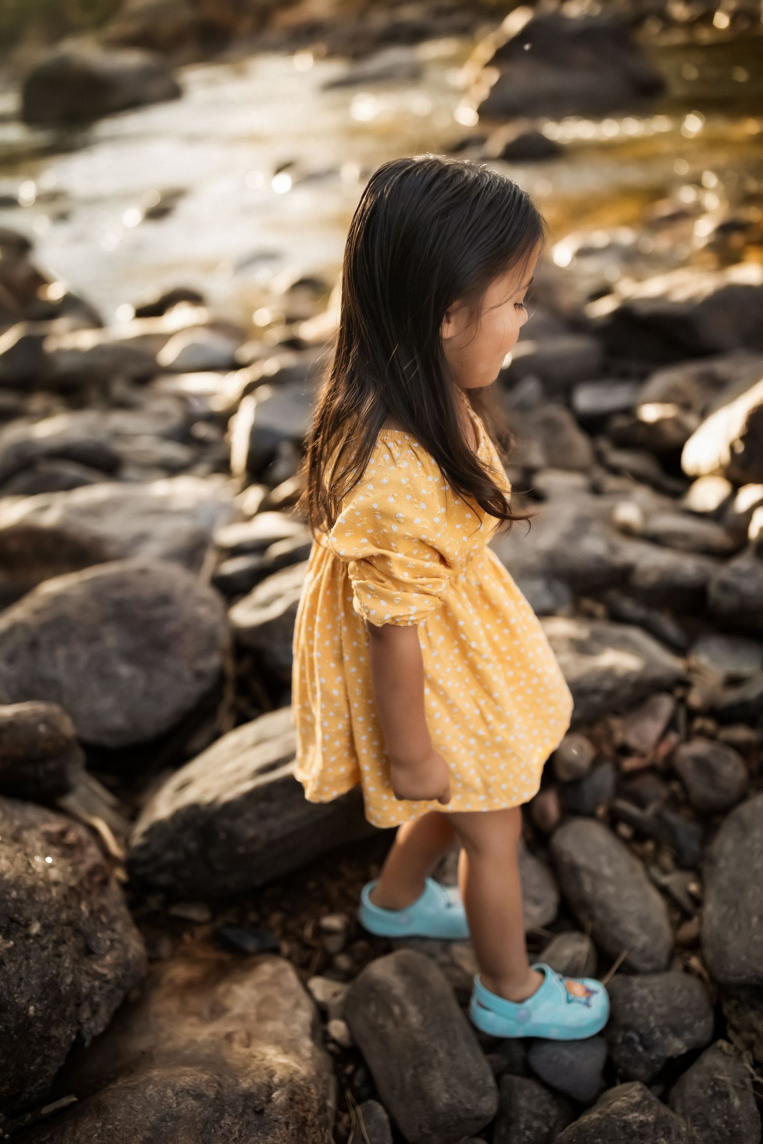 A child in a yellow dress exploring rocky terrain wearing blue shoes.
