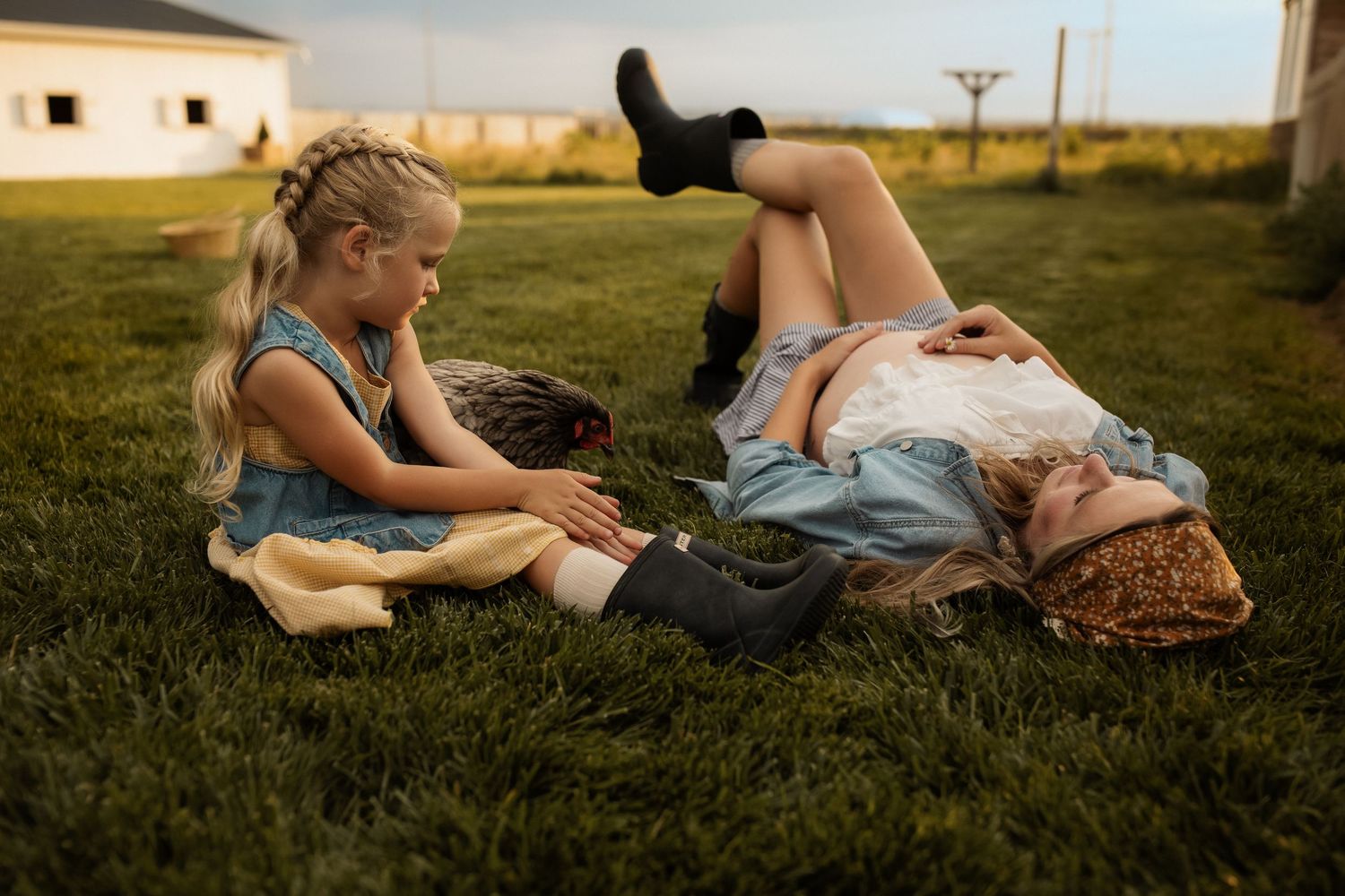 Two people relax together on green grass during a warm summer evening in a rural setting.