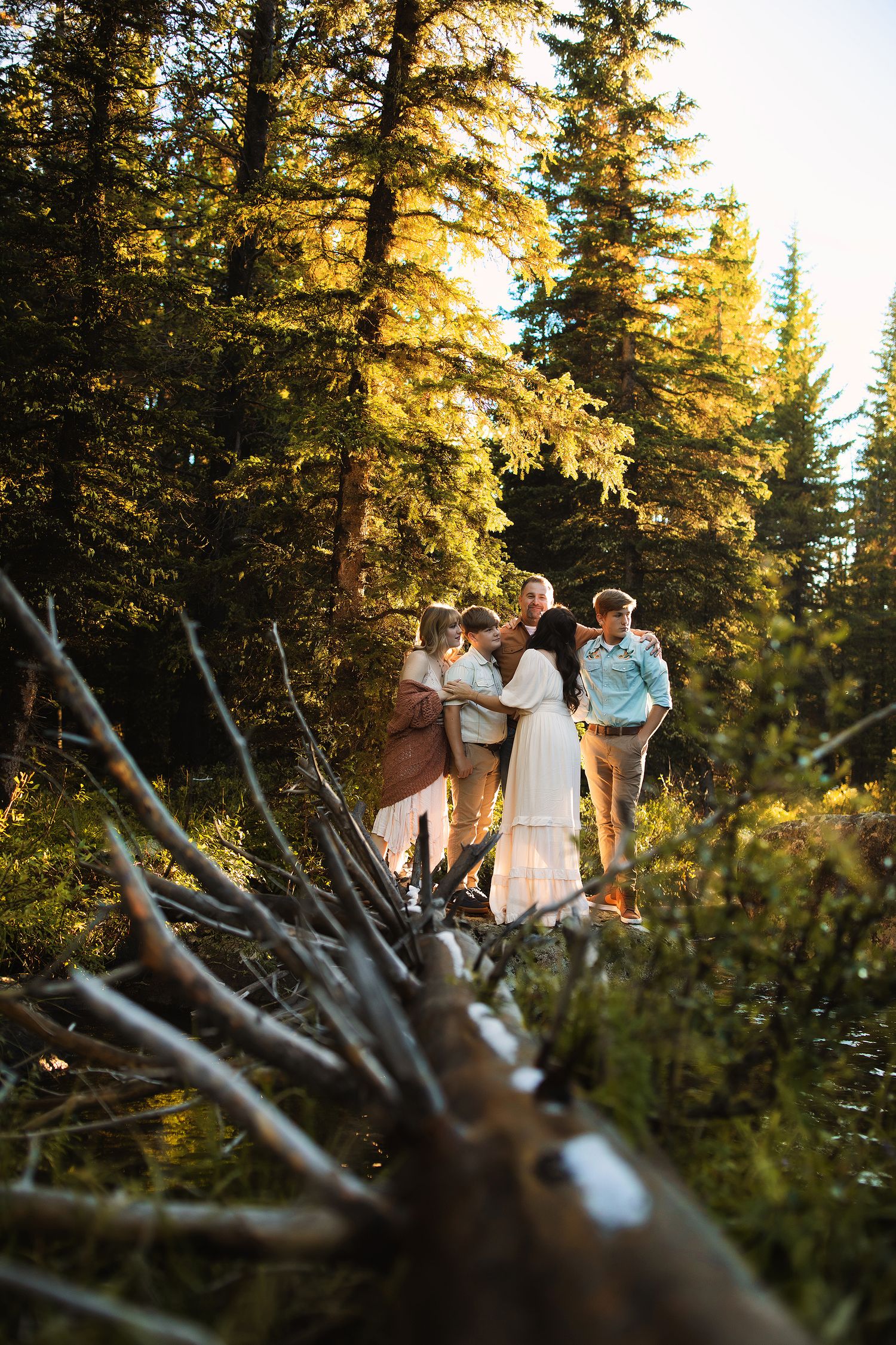A small group explores a sunlit mountain forest trail with evergreen trees casting golden light through branches.