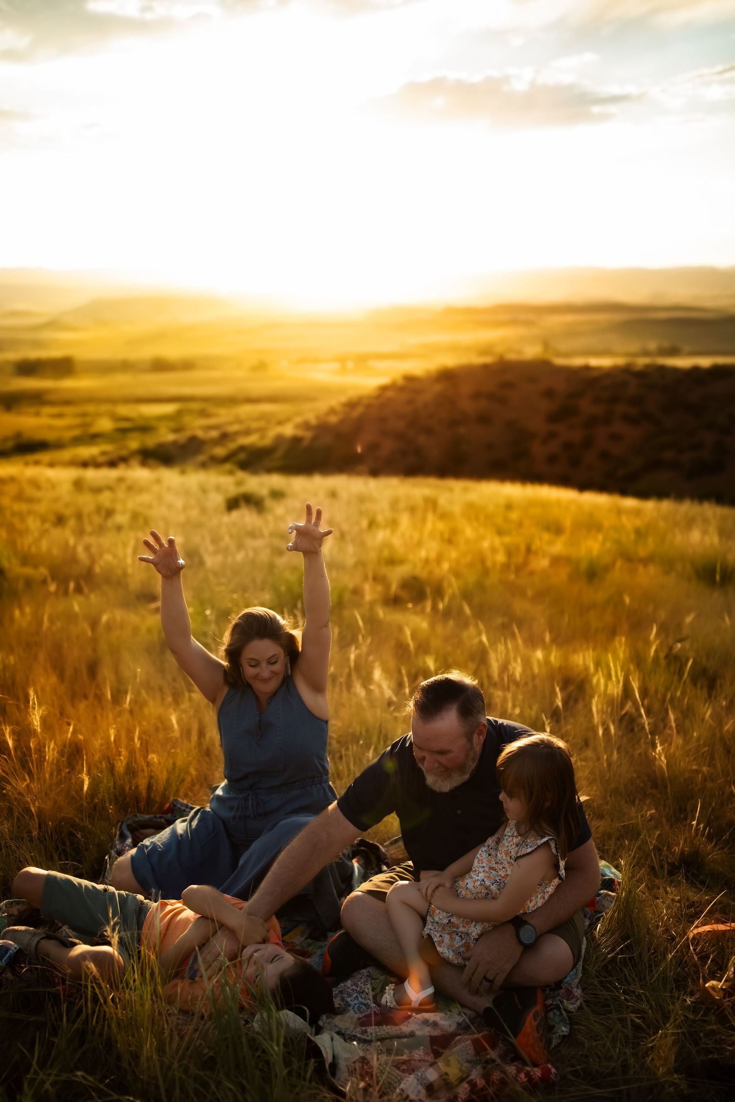 Family enjoying a golden sunset together in a grassy field with mountains in the background.