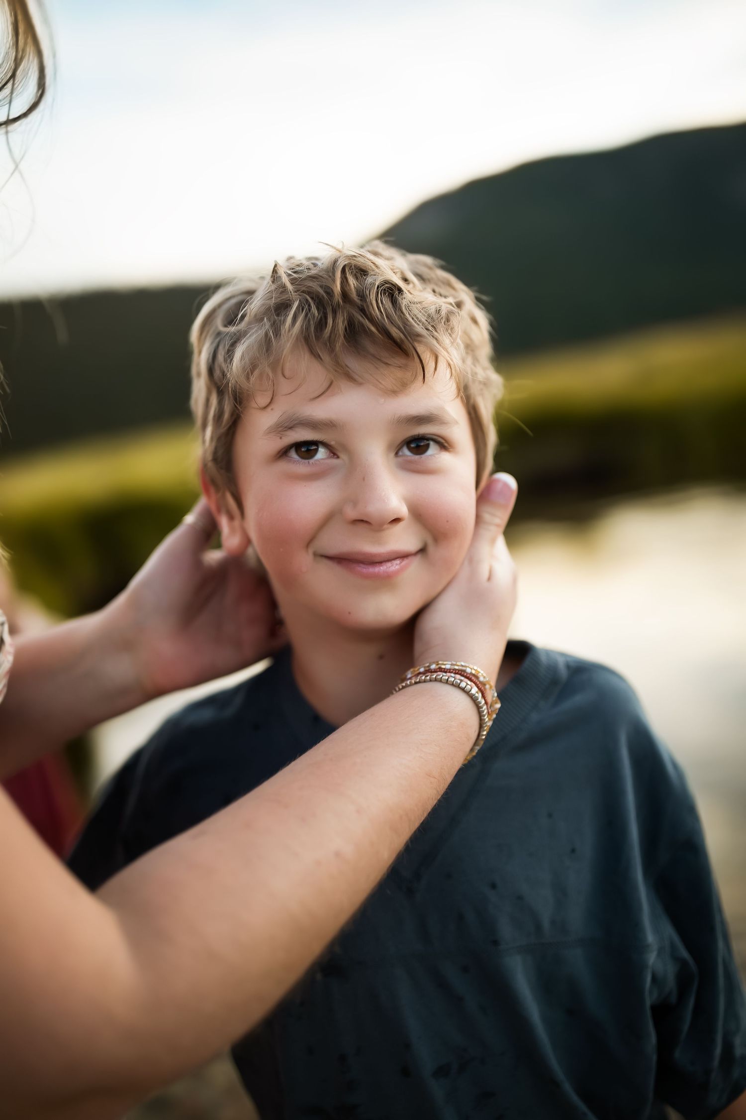 A tender moment captured outdoors as hands gently touch the sides of a child's smiling face.