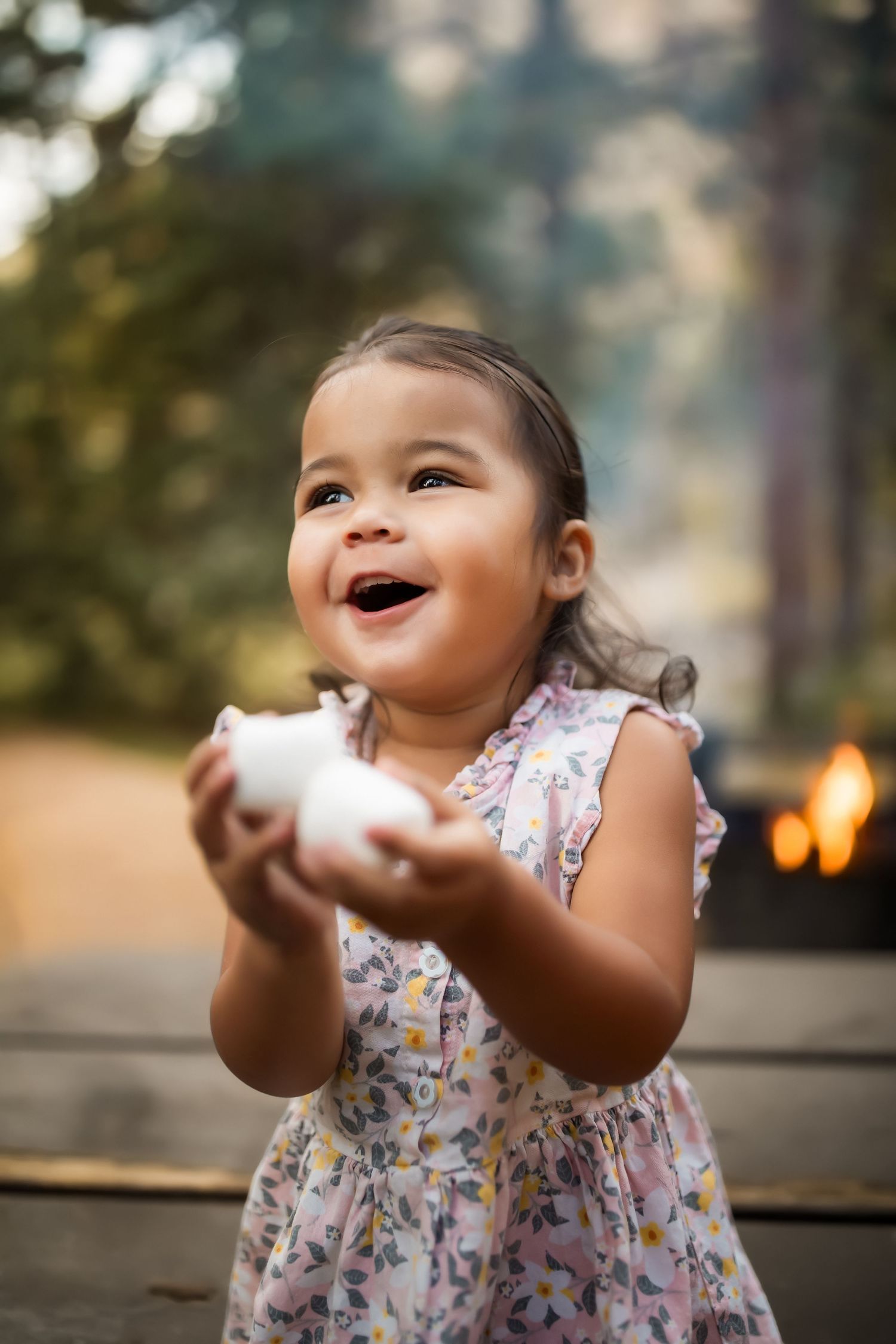 Young child in floral dress laughing and playing outdoors during golden hour.
