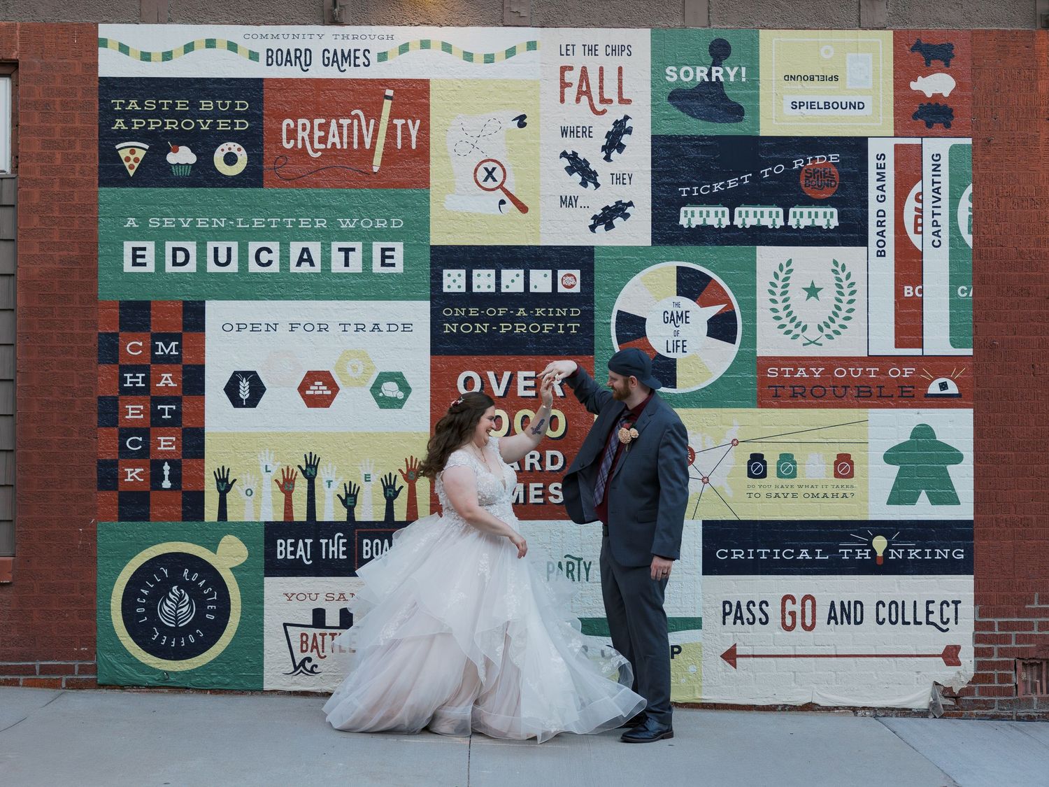 Bride and groom posing in front of a colorful educational board games mural at their wedding.