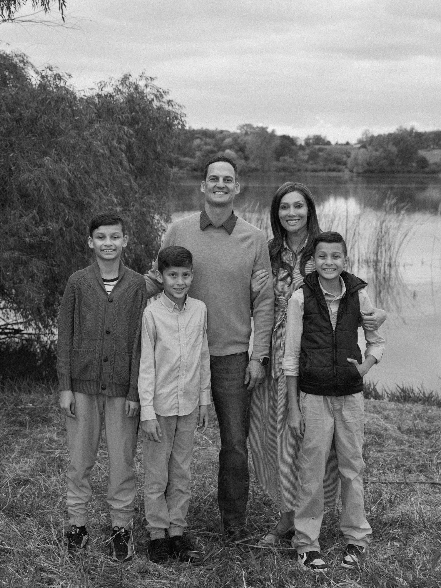 Black and white family portrait by a lake with casual clothing and natural poses.