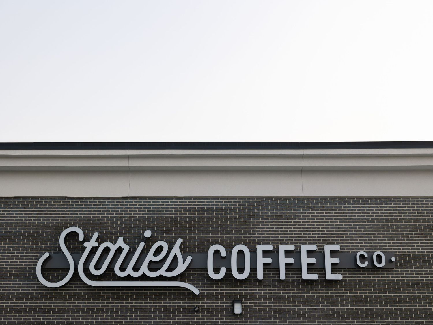 Stories Coffee Co. signage on a brick building exterior with white lettering against a gray sky.