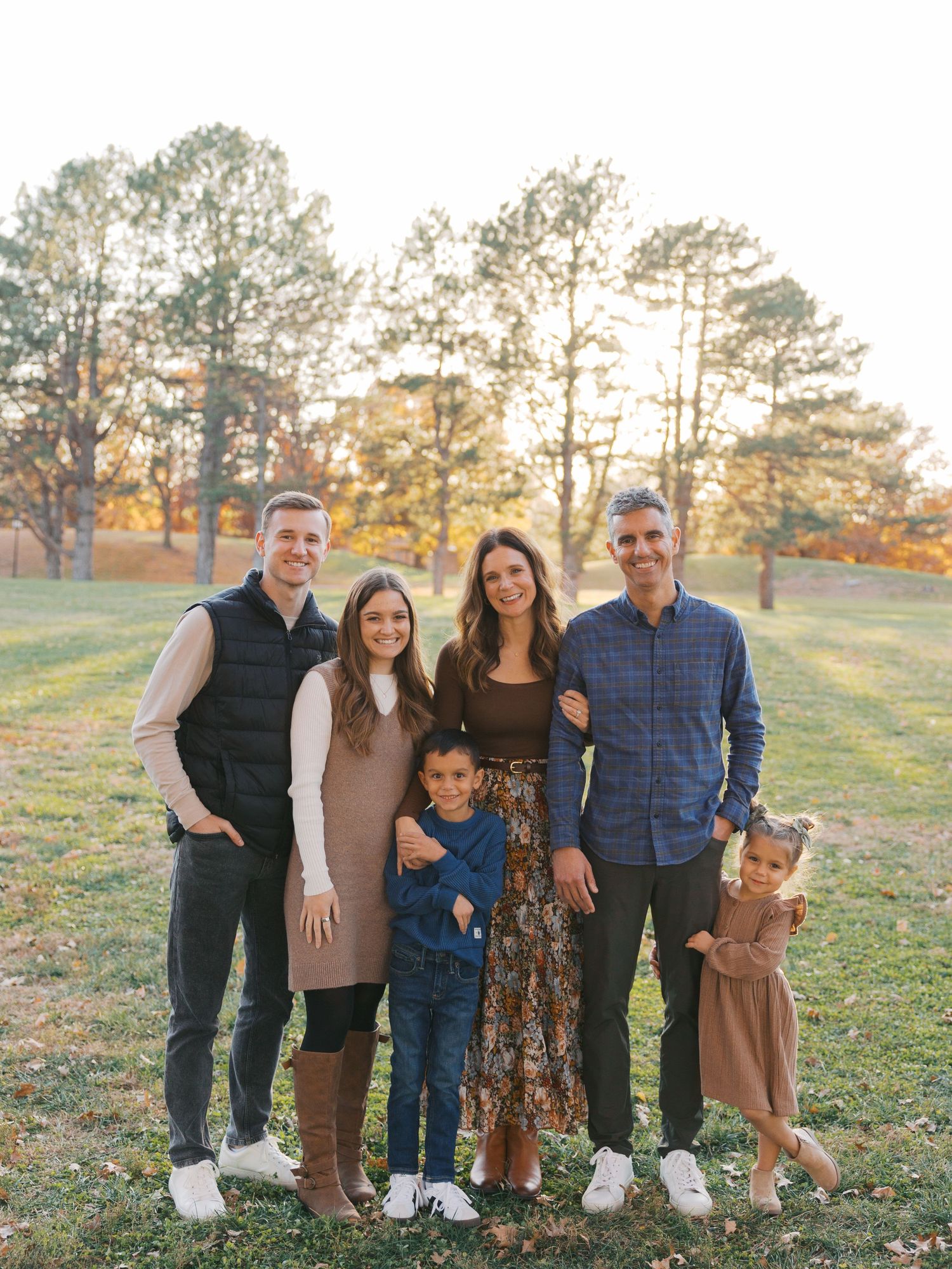 Family of six posing together outdoors in a park during golden hour fall season photo session.