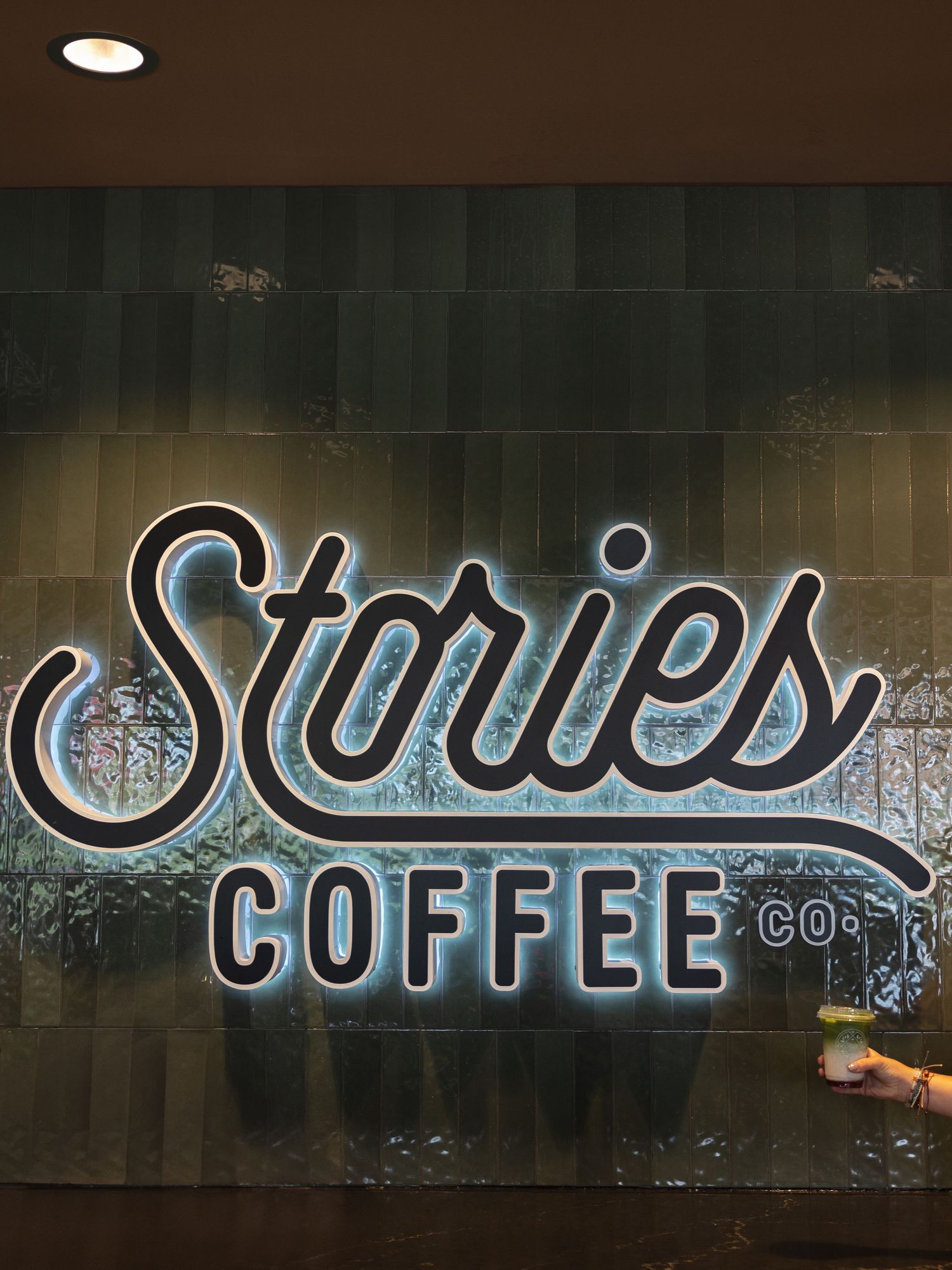 Stories Coffee Co. illuminated logo sign displayed on a dark tiled wall inside a modern coffee shop.