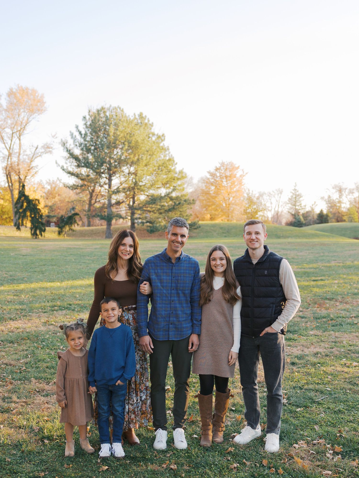 Family group portrait outdoors in casual wear during golden hour in grassy field.