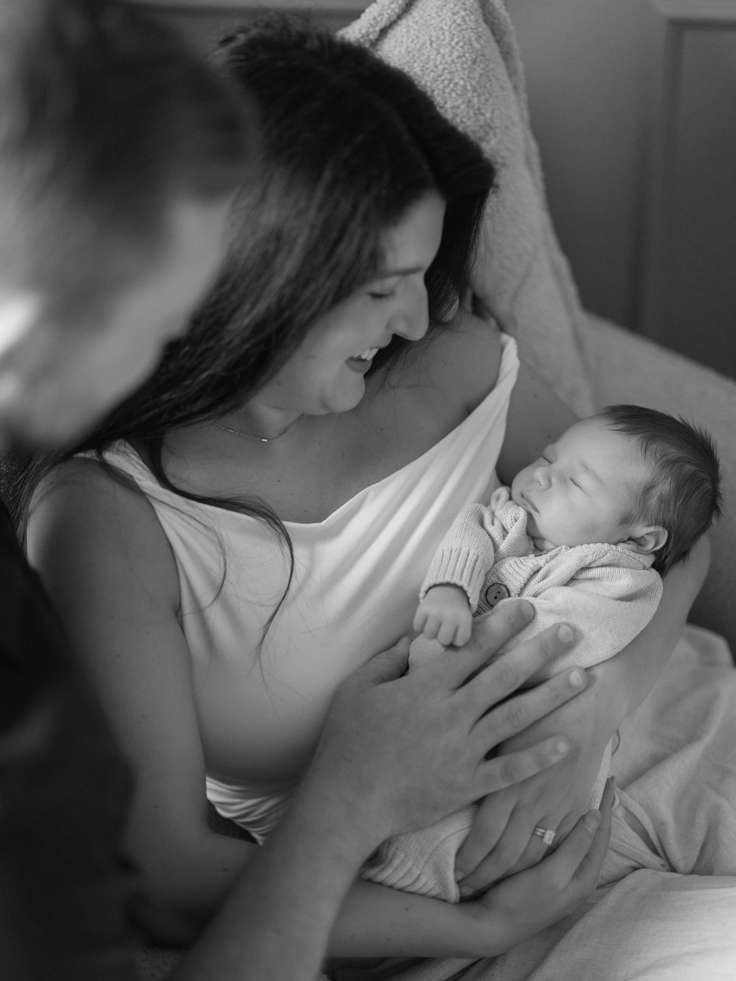 Black and white photo of a smiling mother tenderly holding her newborn baby while another child looks on.