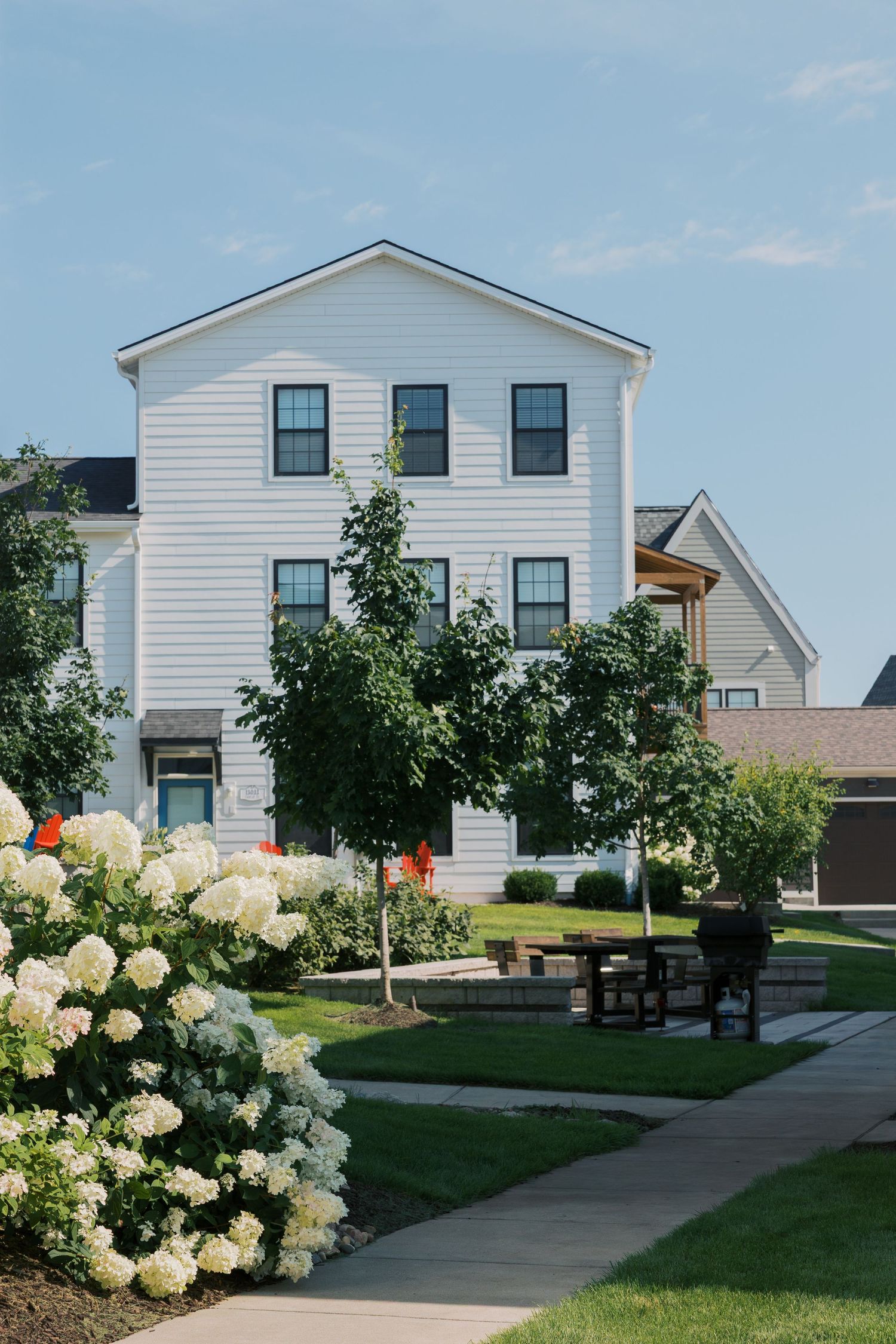 White residential buildings with landscaped pathway and blooming hydrangea bushes.