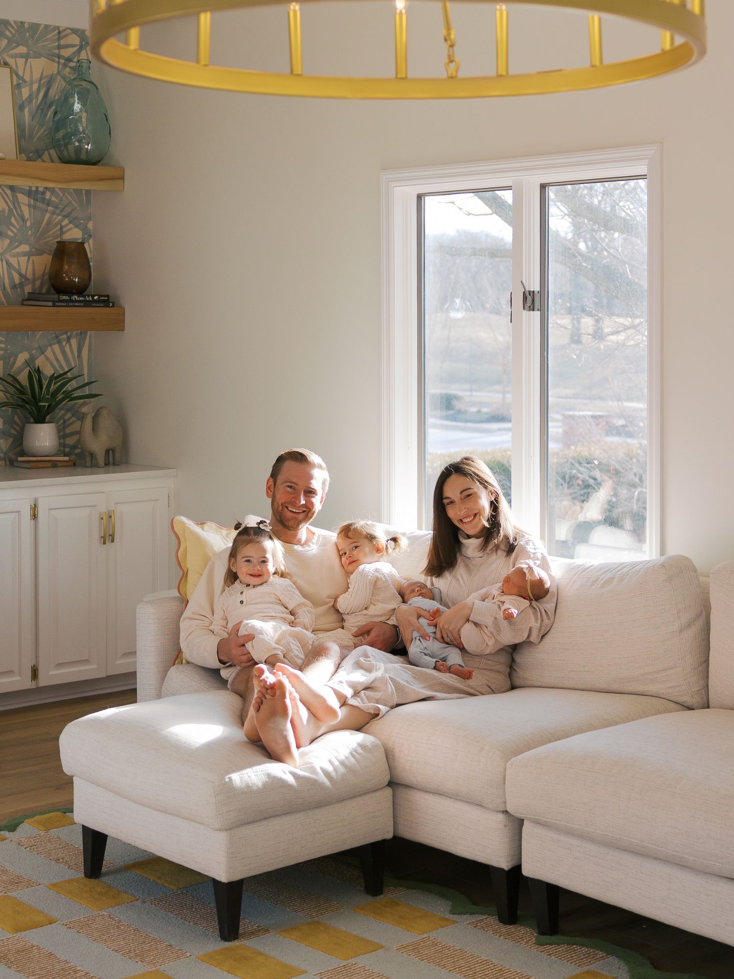 Family relaxing together on white sectional sofa under modern gold light fixture.