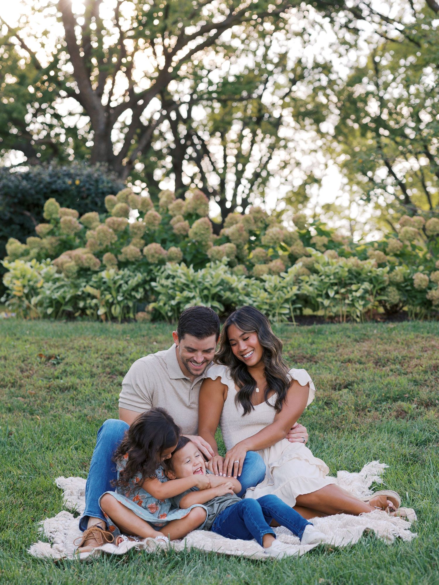 Family relaxing together on blanket in garden with blooming hydrangeas in background.