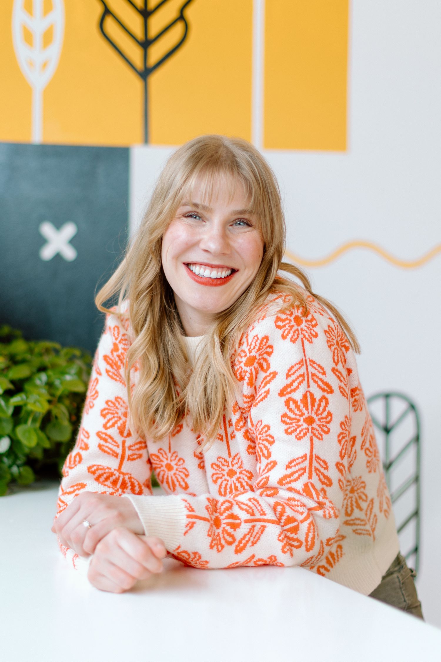 Woman in orange floral dress lying down and smiling against yellow and white backdrop.