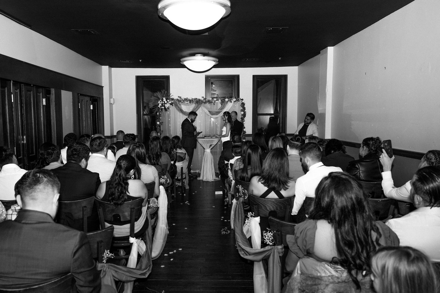 Black and white photo of a wedding ceremony with guests seated in rows as couple stands at the altar.