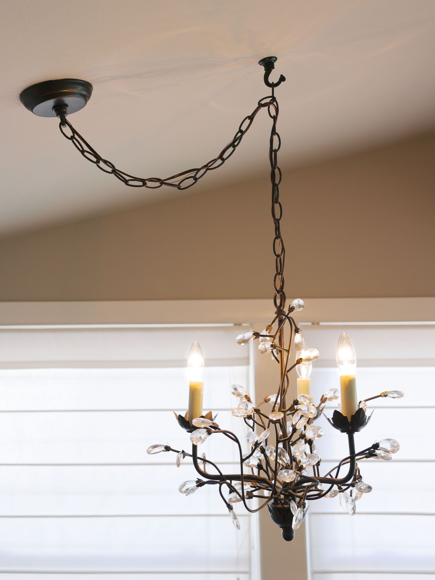 Elegant bronze chandelier with crystal details suspended by decorative chain against white ceiling.