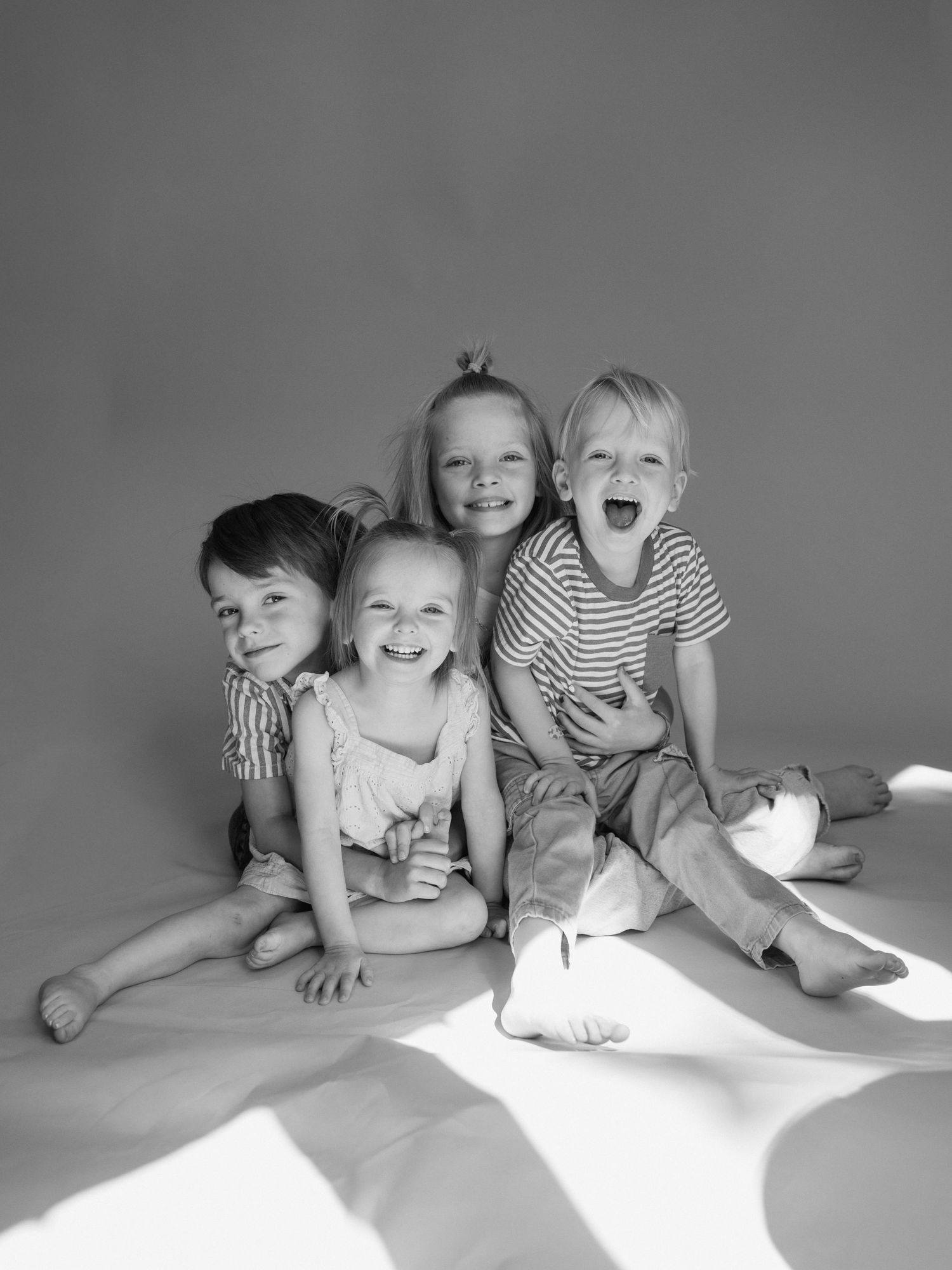 Black and white studio portrait of four happy young children sitting together, smiling and laughing.