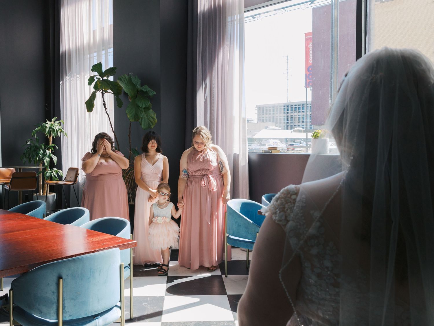 Bridesmaids in pink dresses react emotionally during a bridal first look reveal in a modern venue.