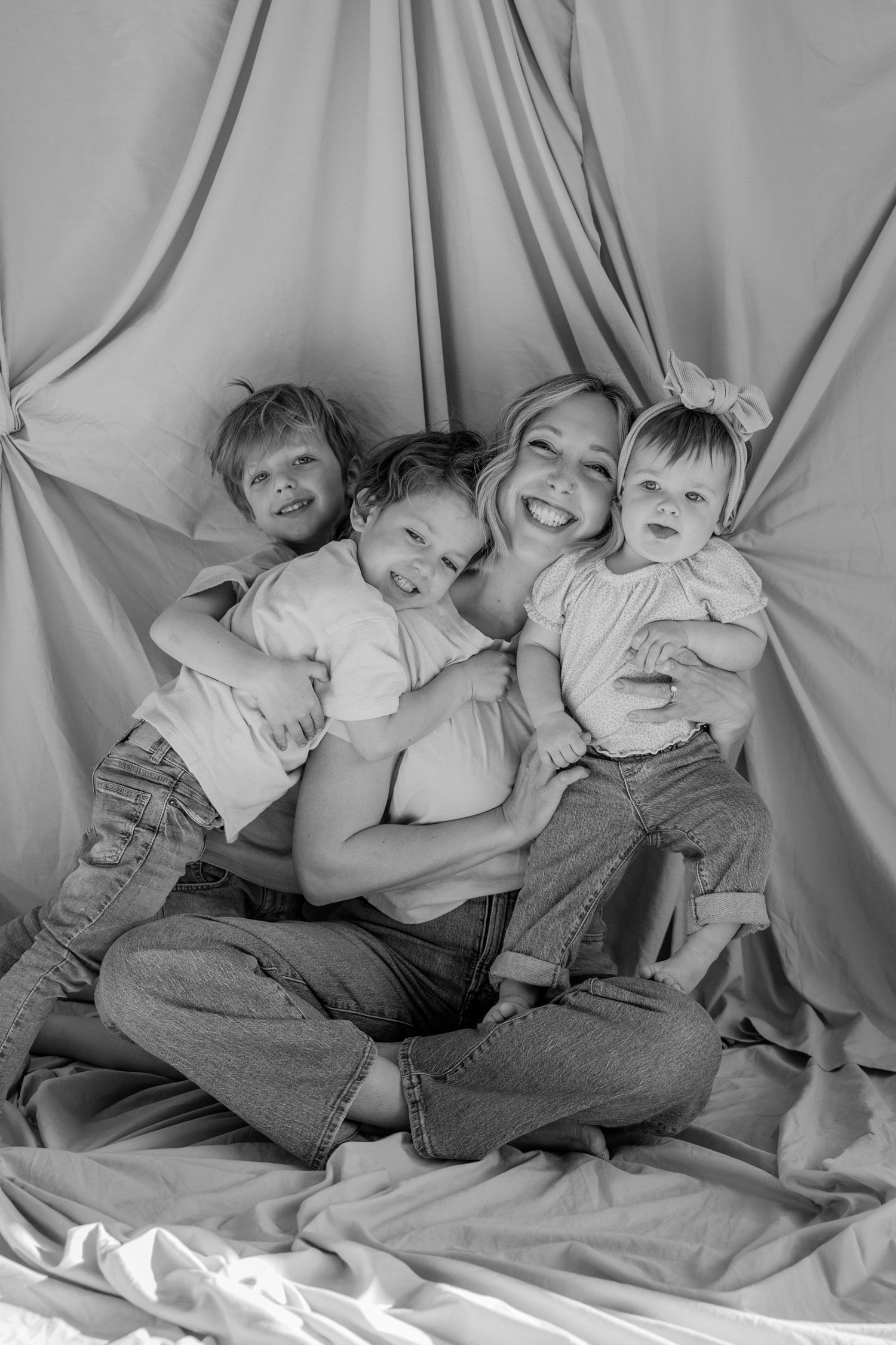 Black and white portrait of family members lying together on light colored fabric.