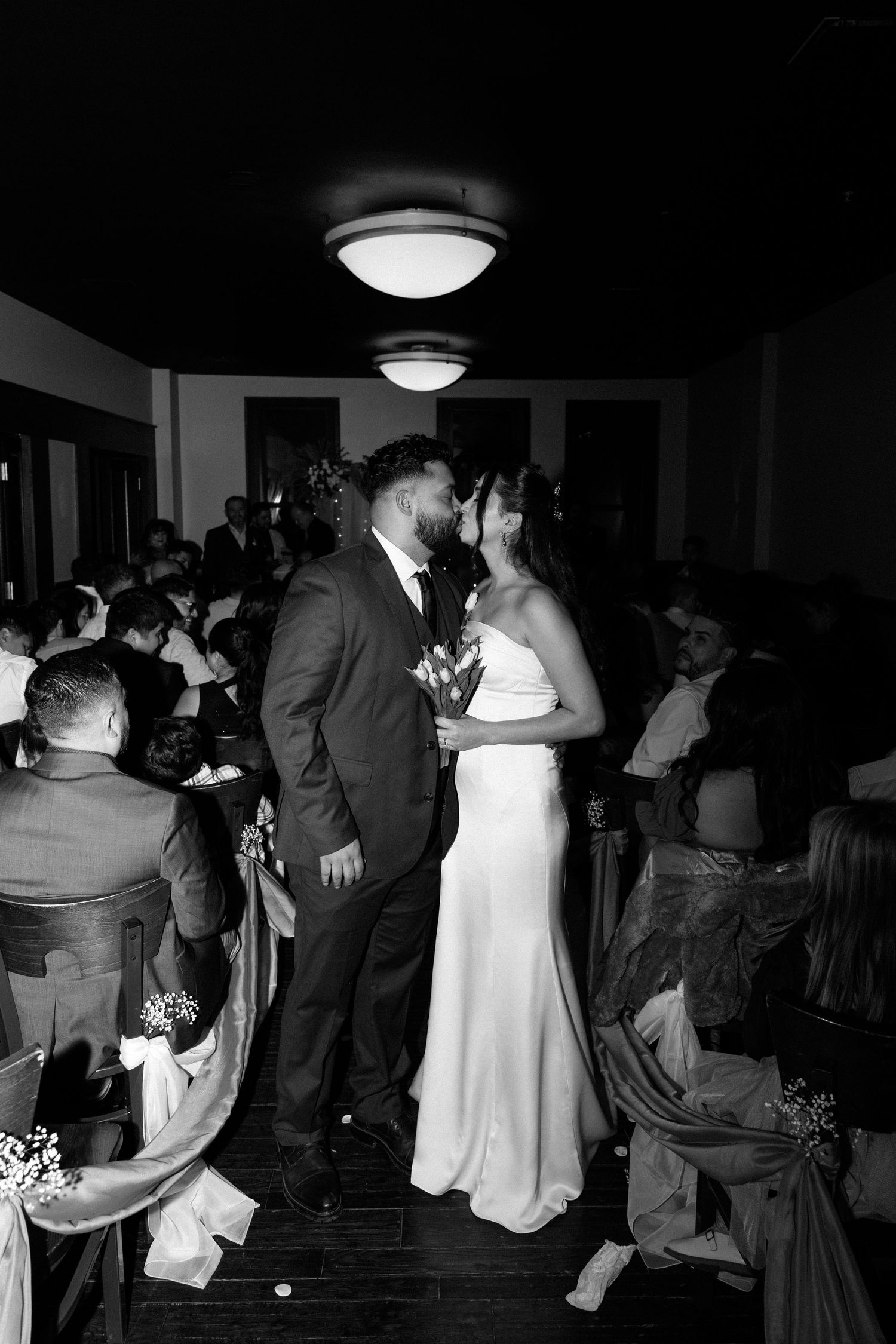 Black and white photo of a couple sharing their first kiss as newlyweds at the altar during their wedding ceremony.