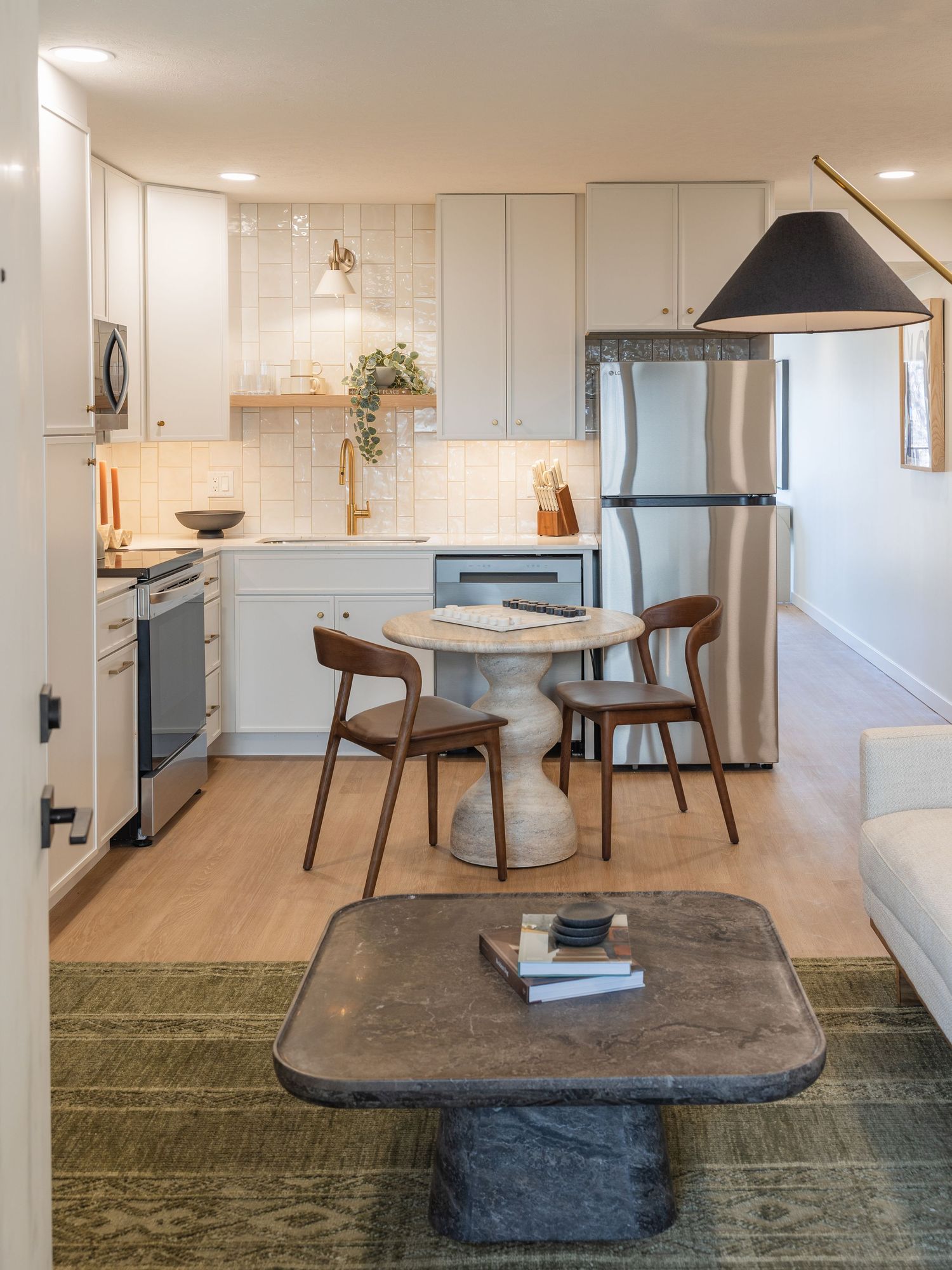 Modern open-plan kitchen and dining area with white cabinets, marble table, wooden chairs, and green patterned rug.