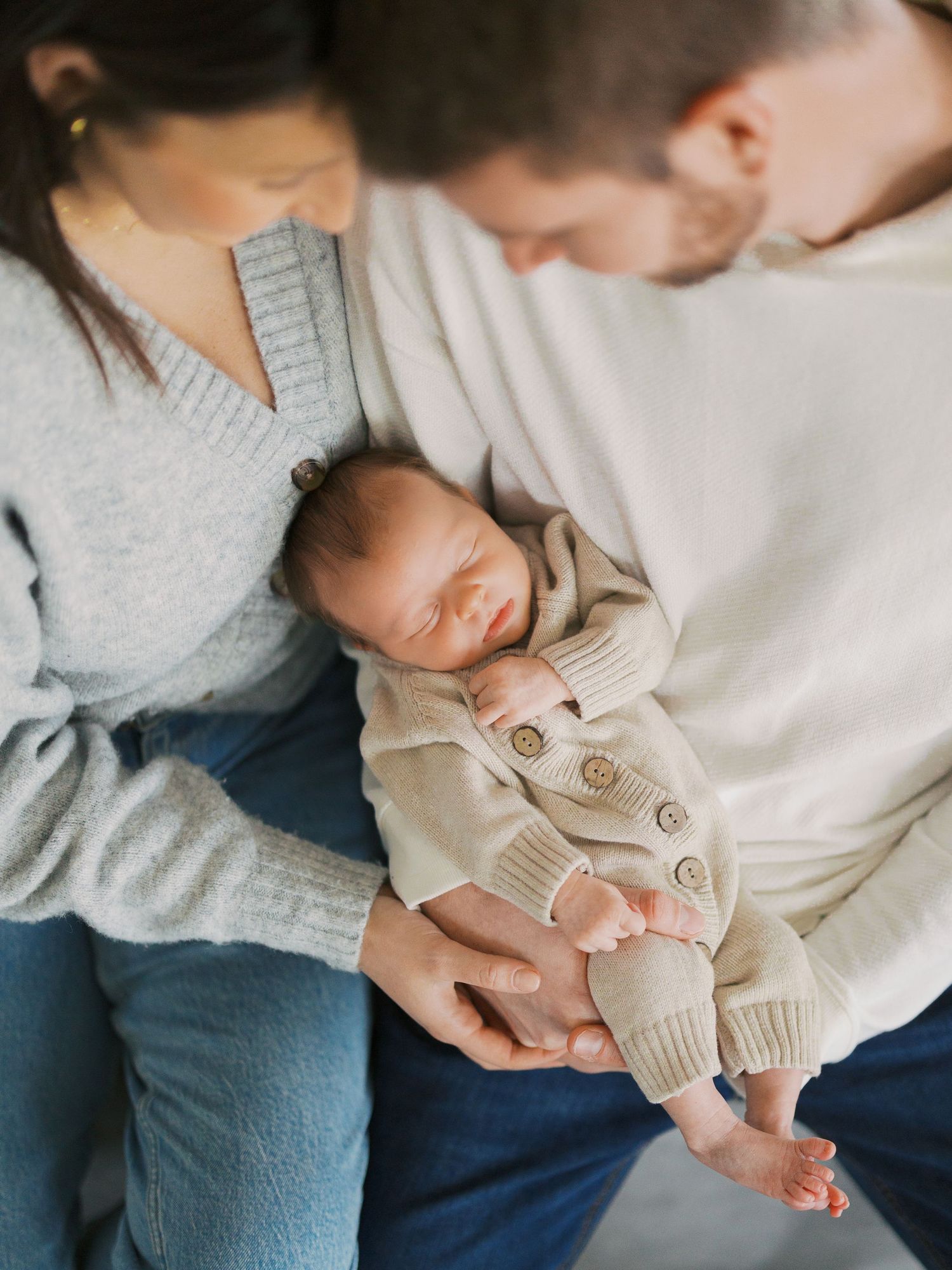 Tender moment with newborn baby in cozy knit outfit surrounded by loving embrace.