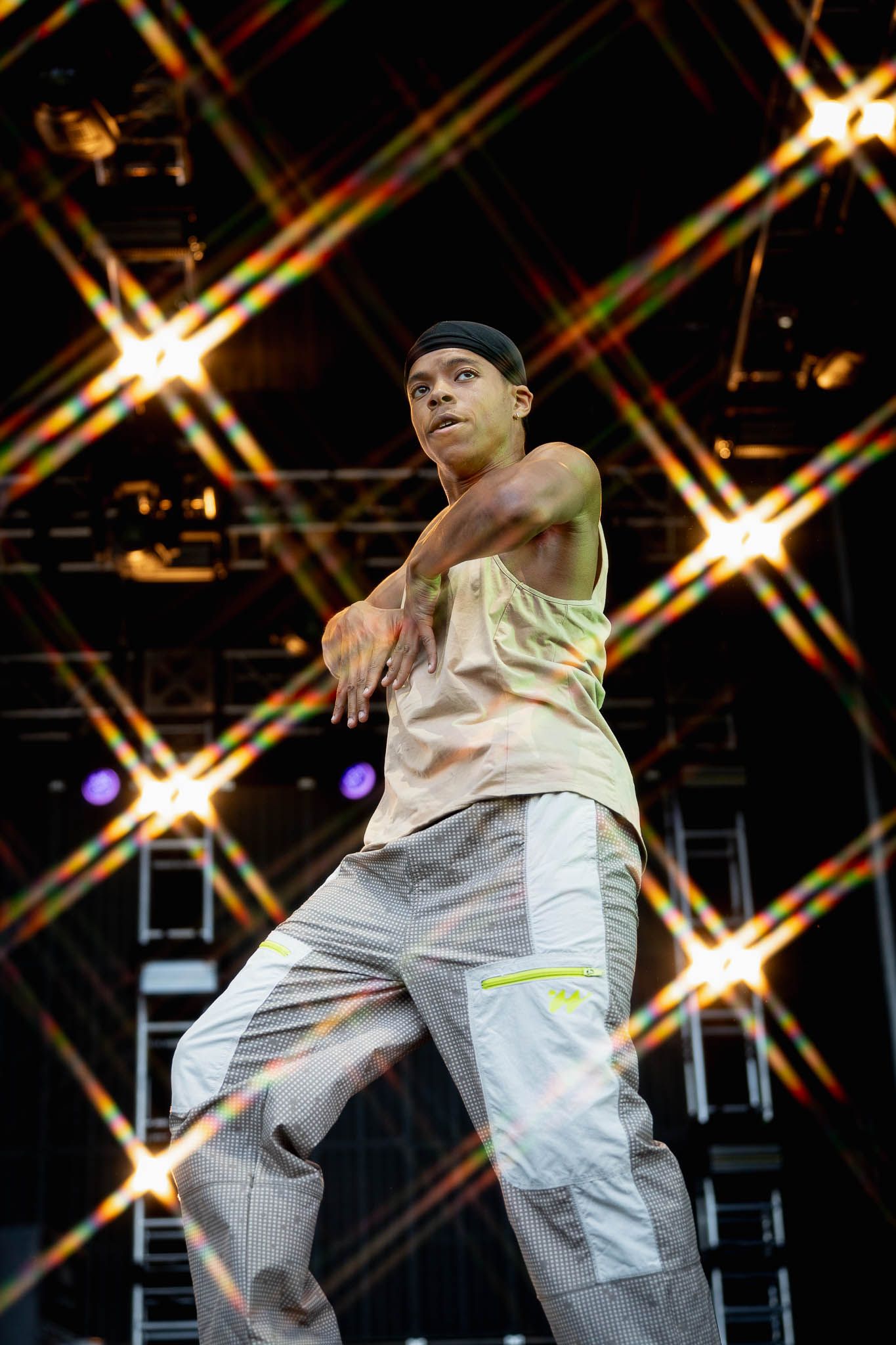Dancer in casual outfit performs against geometric light pattern backdrop on concert stage.