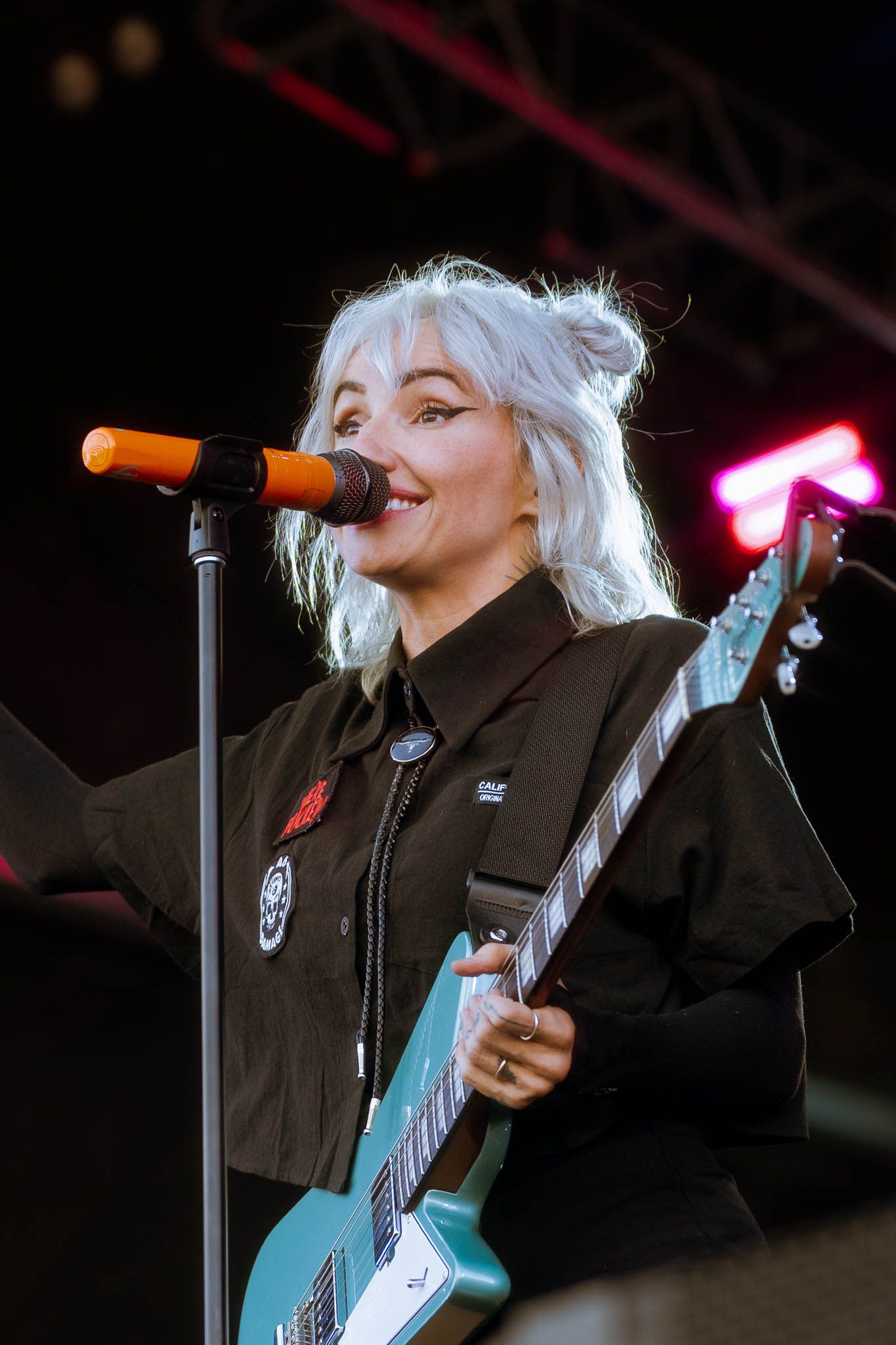 Lights performs with microphone while playing teal guitar under dramatic stage lighting.