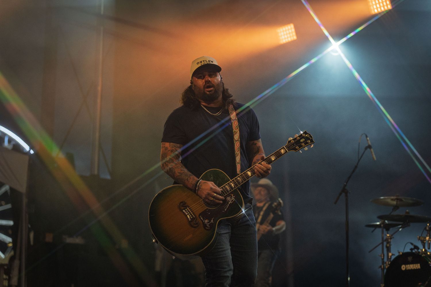 Country artist Koe Wetzel performing on stage with dramatic blue and orange lighting effects.