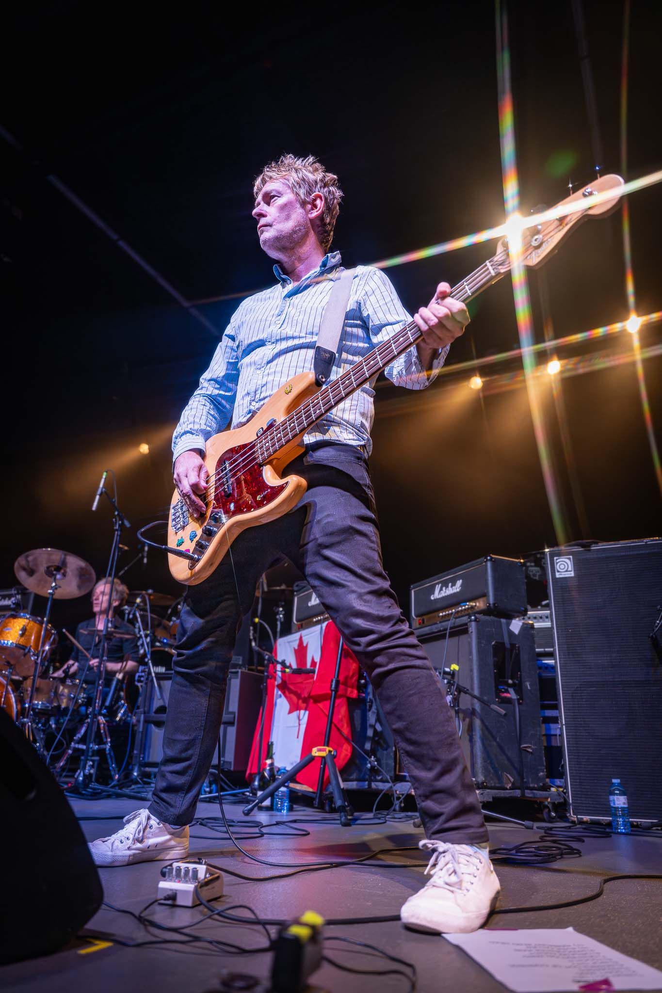 Bass guitarist performing on stage with bright overhead lighting and equipment.