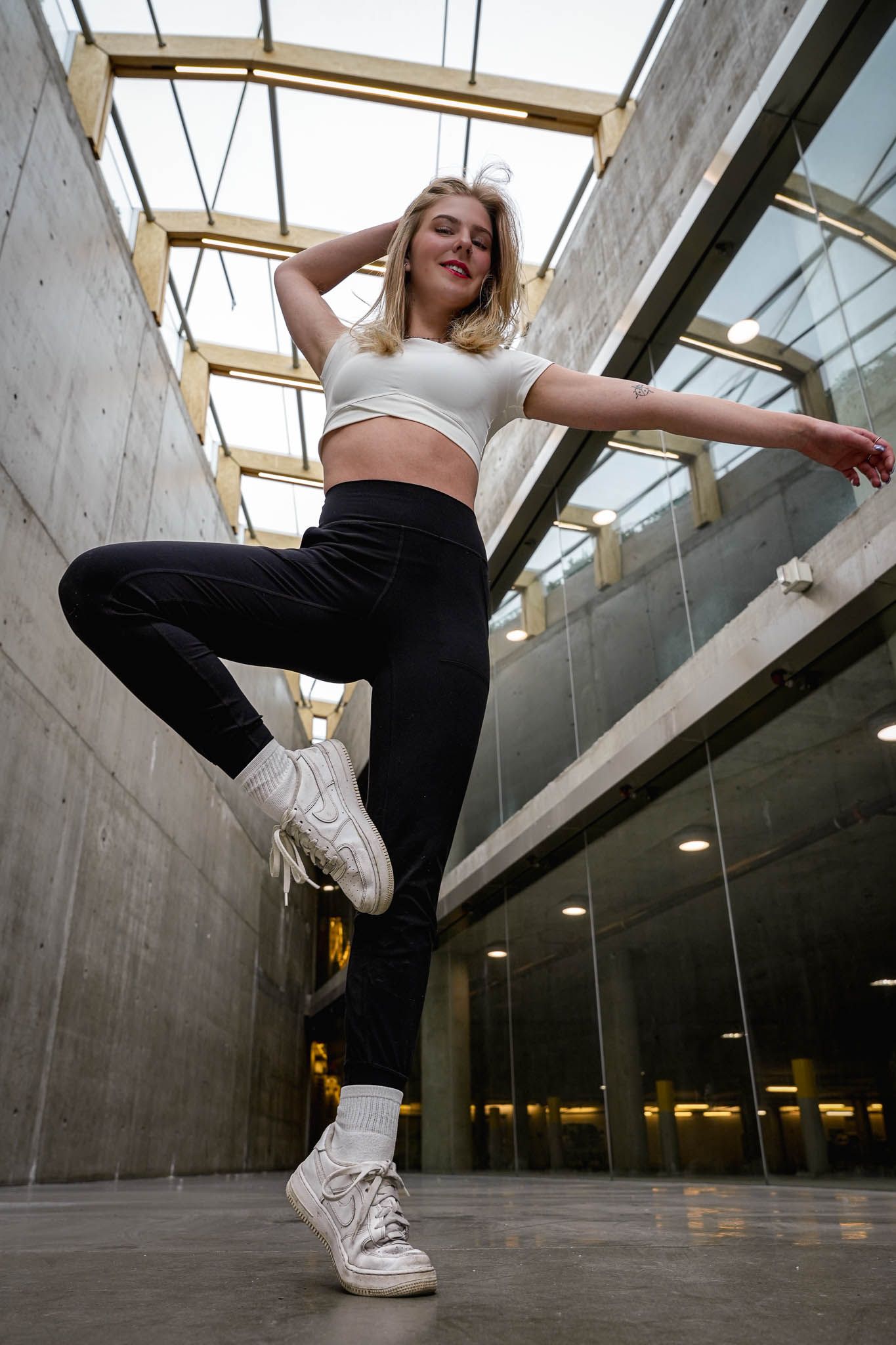 Dancer performs high kick move in concrete hallway with skylights.