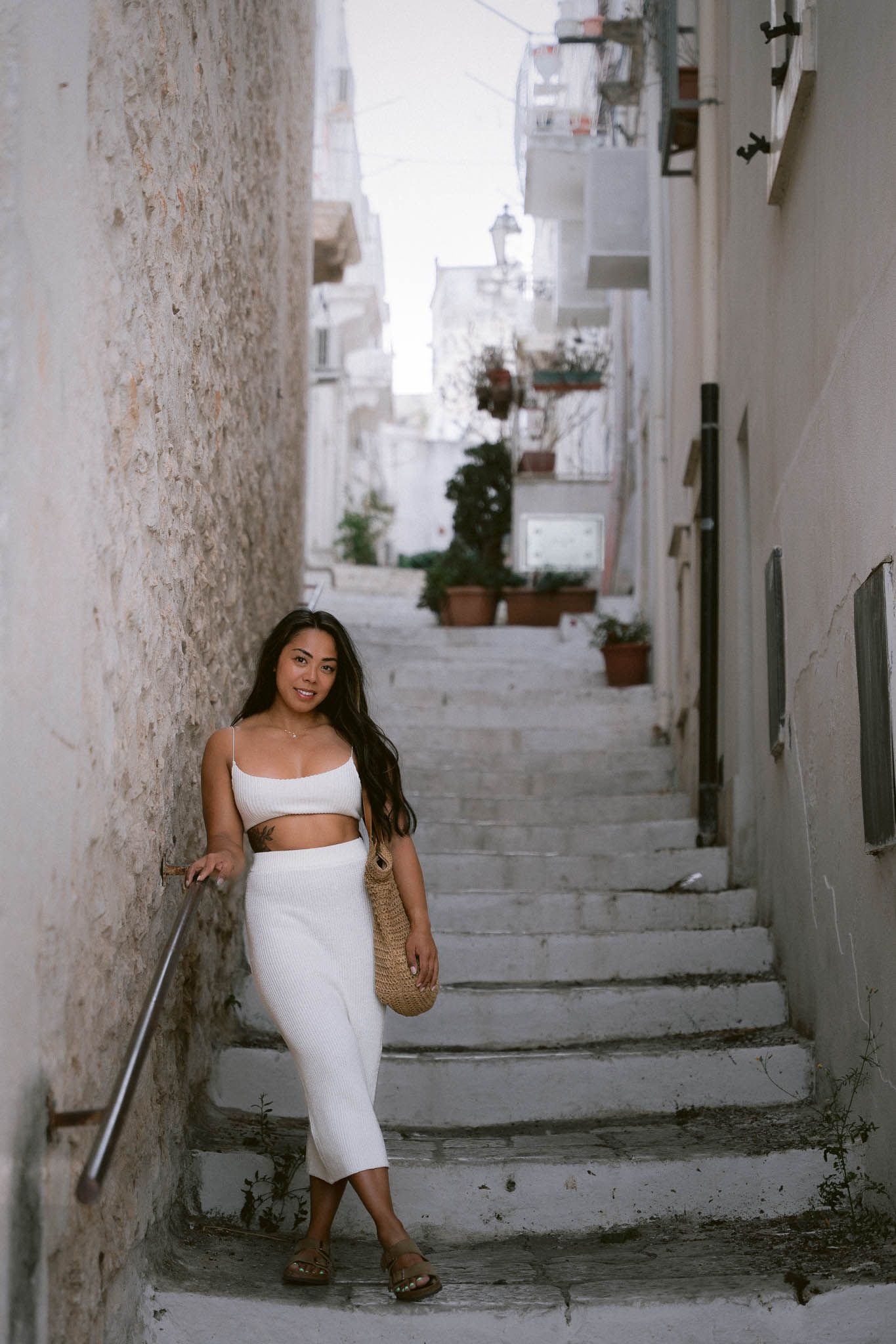 A white two-piece outfit worn on a scenic Mediterranean stairway with potted plants and whitewashed walls in Cisternino Italy