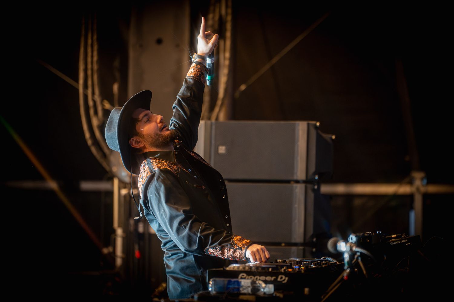 DJ Alesso working the turntables in moody lighting at a nightclub performance.