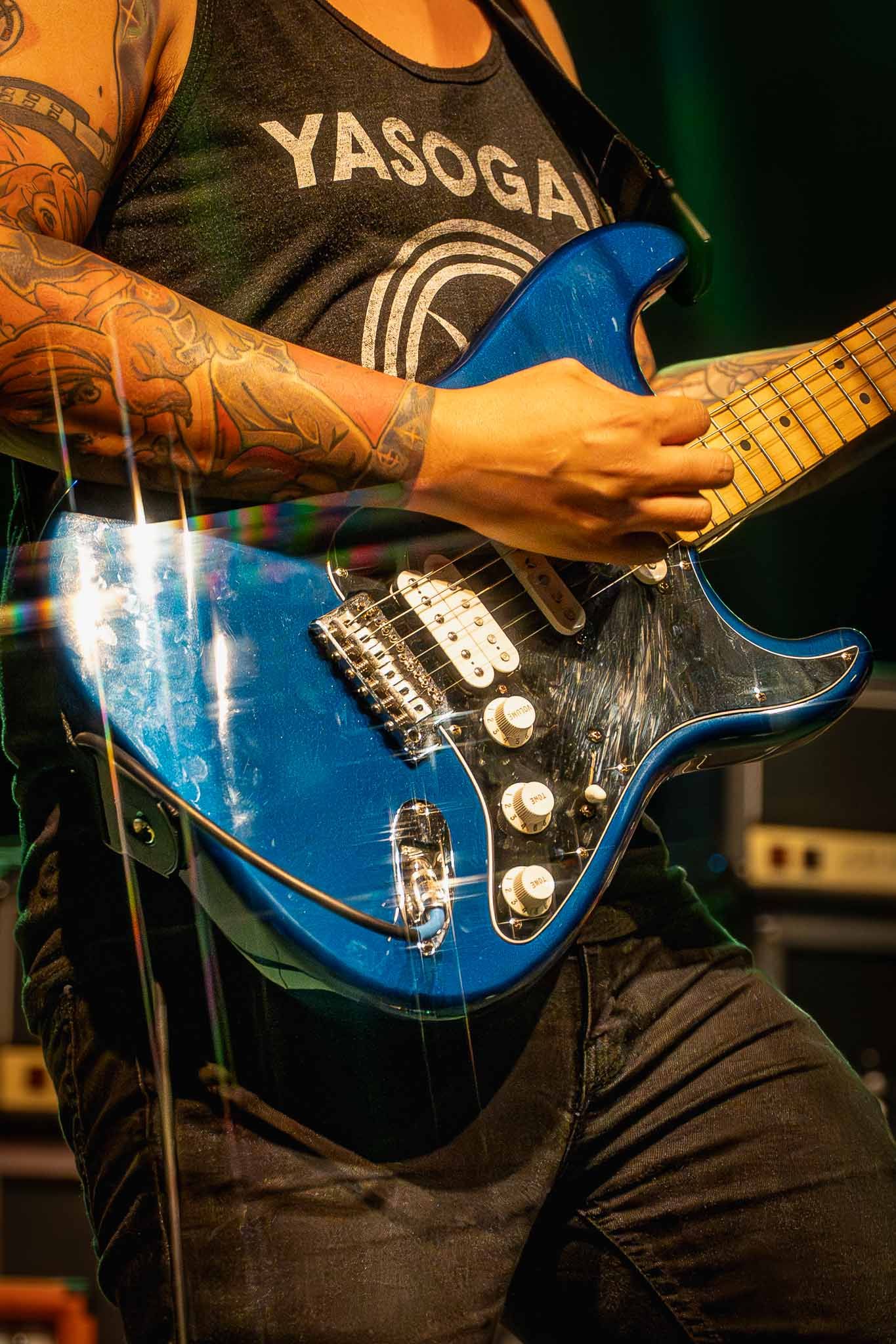 Close-up shots of blue electric guitar being played by tattooed hands during performance.
