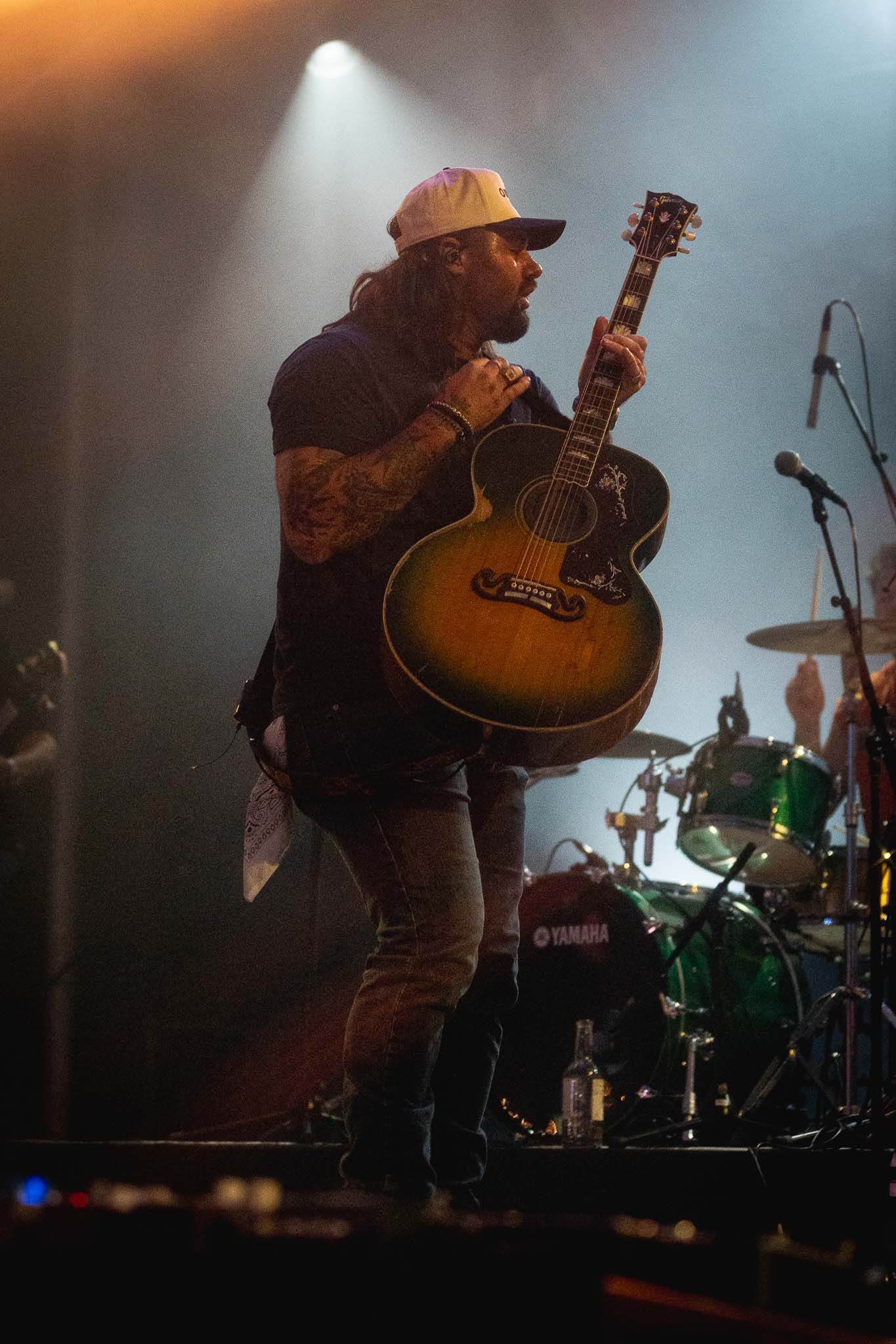 Koe Wetzel with guitar performing on a smoky stage with drum kit visible in background.